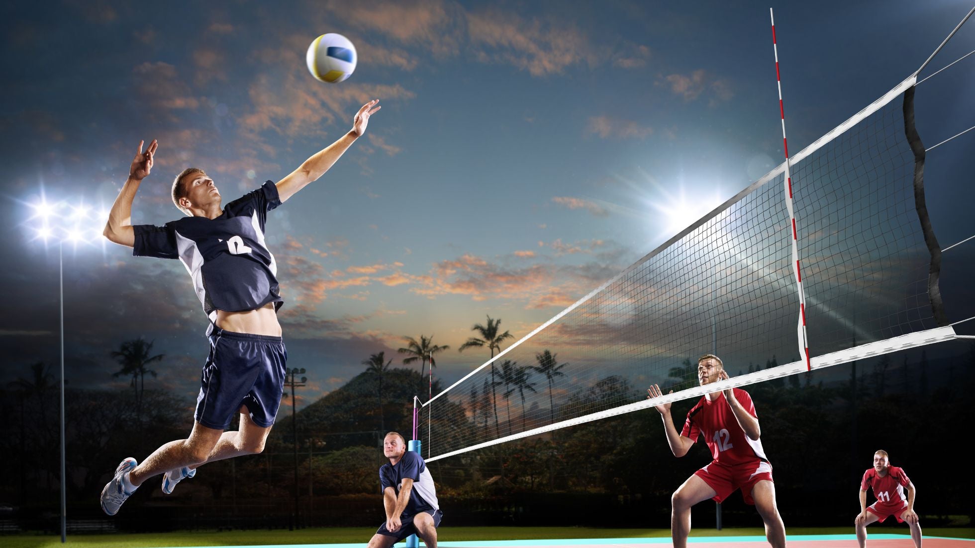 Volleyball game in progress with players on a court at night.