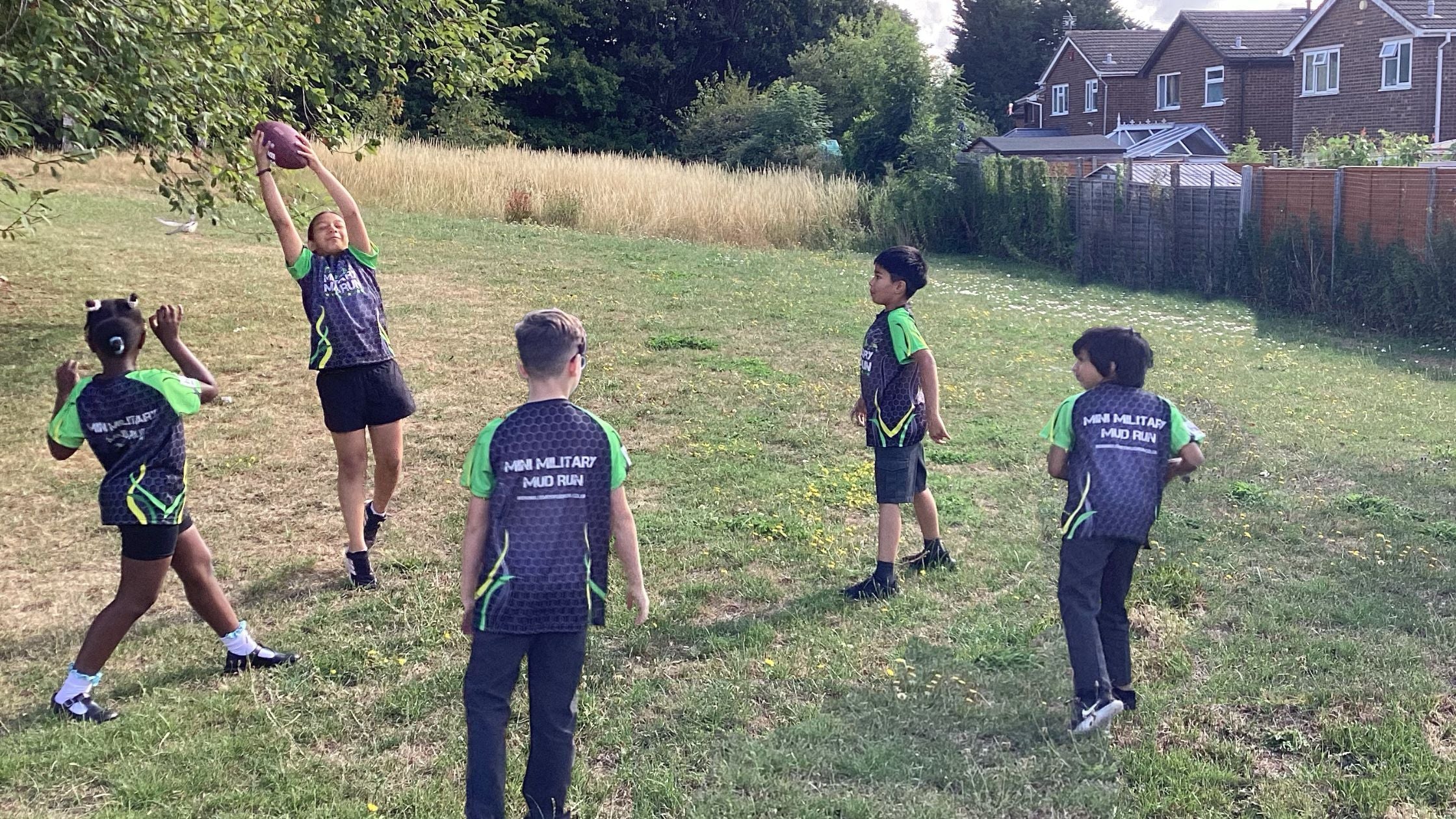 Children playing a game of catch in a grassy field with houses in the background