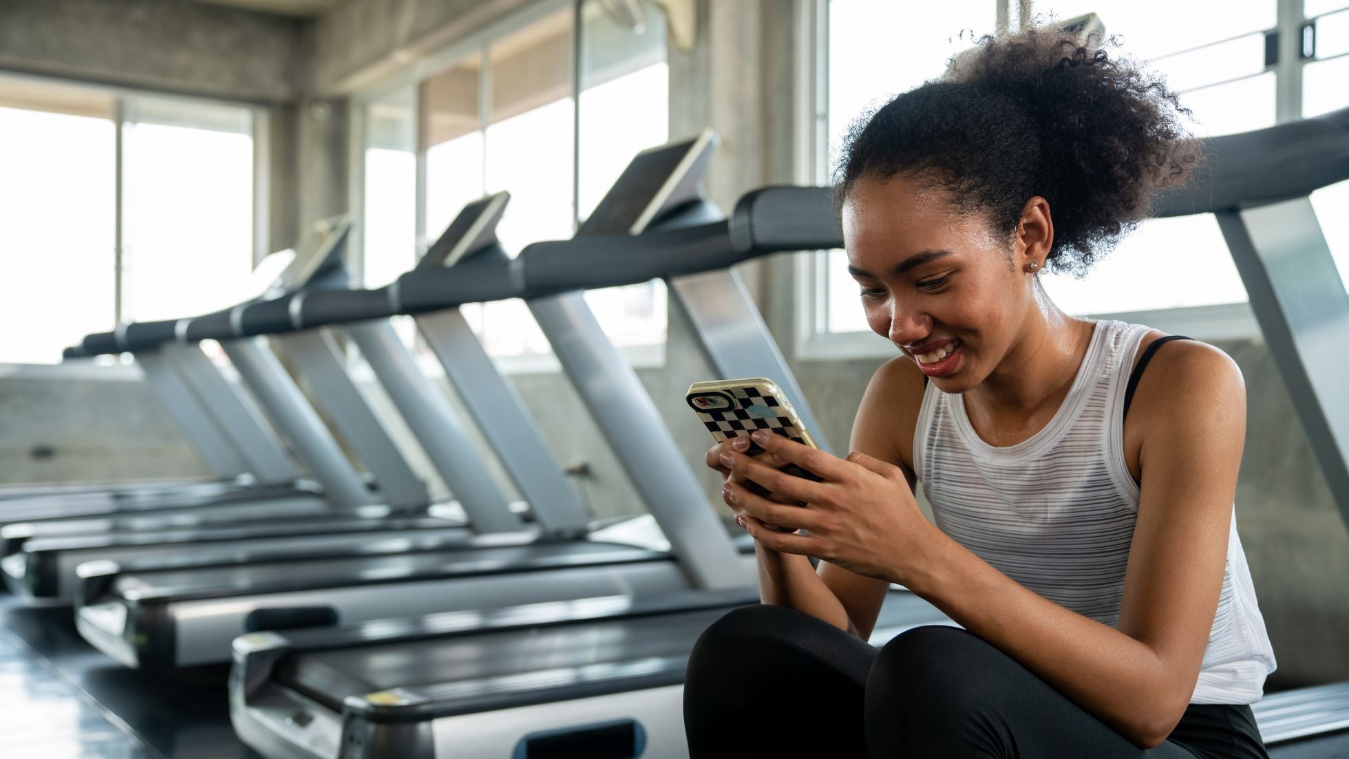 Woman using a smartphone in a gym setting with treadmills in the background