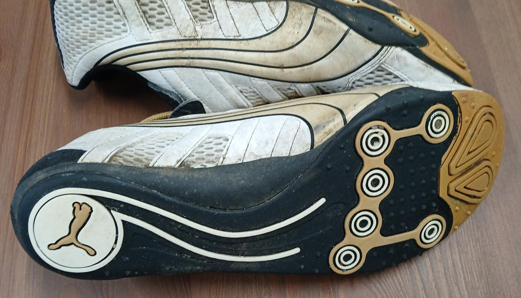 Side view of used men's Puma running trainers with white mesh upper and gold detailing on wooden floor