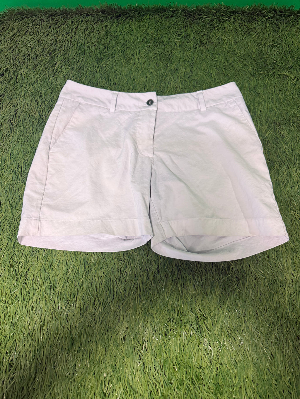 Front view of white women's golf shorts laid flat on grass, showing pockets and button fastening