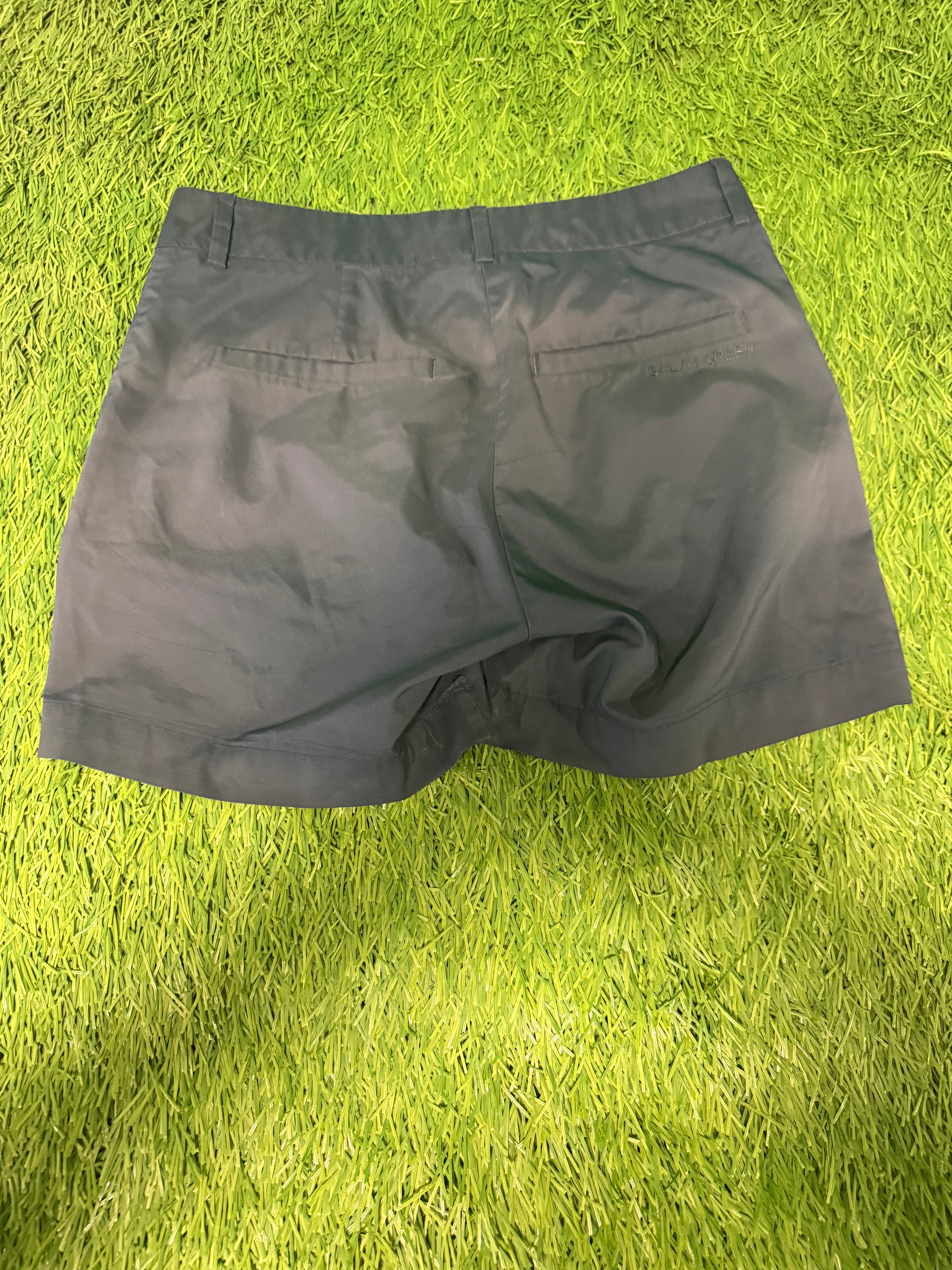 Rear view of black Galvin Green golf shorts showing back pockets and logo detail on grass