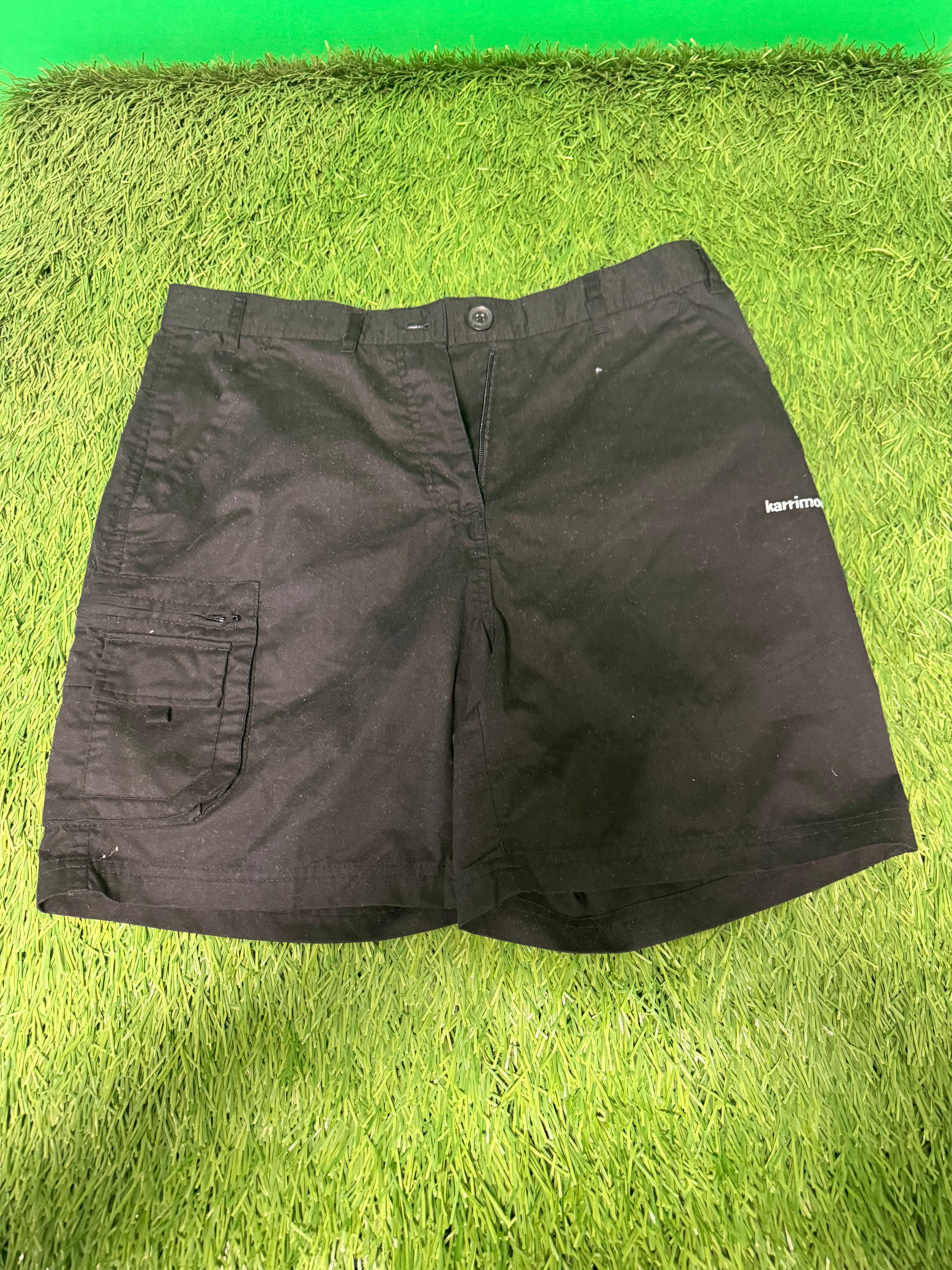 Front view of Karrimor black utility shorts with zippered pocket laid on green grass