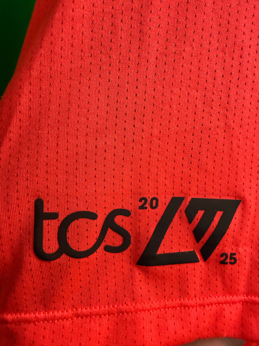 Close-up of red breathable mesh fabric with black tcs 2025 and geometric logo printed on the front