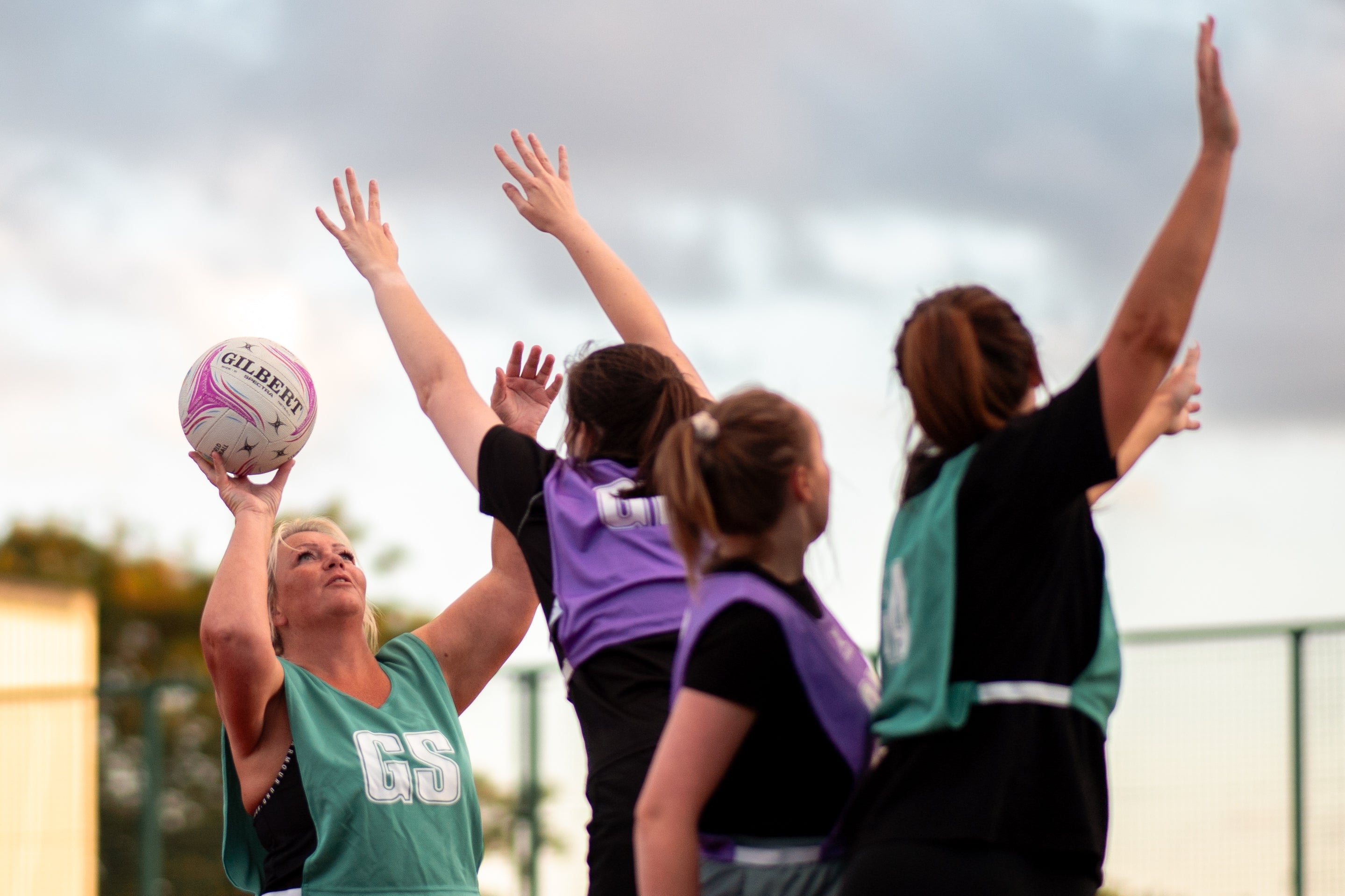 Group of women playing netball on an outdoor court with a cloudy sky.