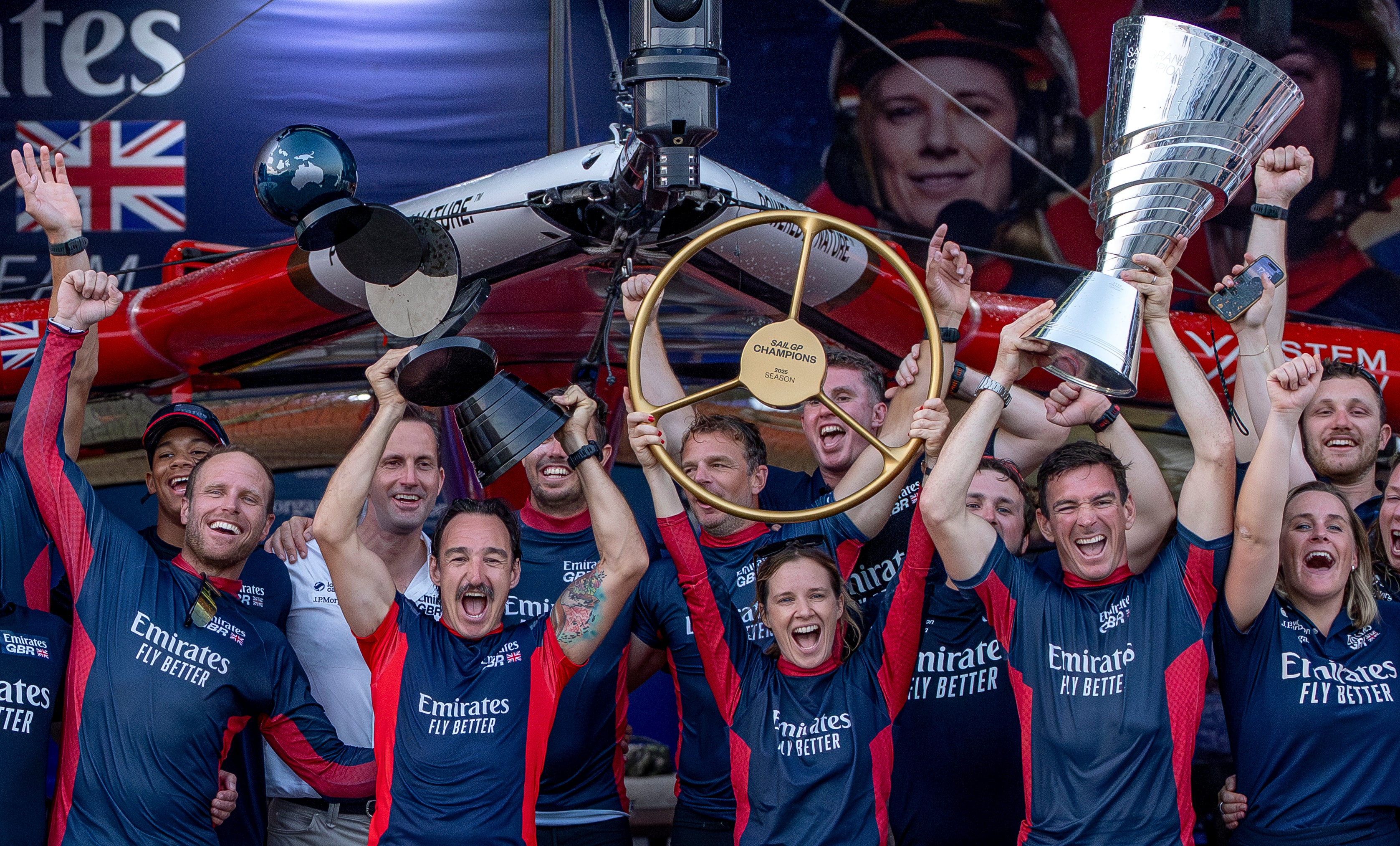 Team celebrating with trophies and a large British flag in the background