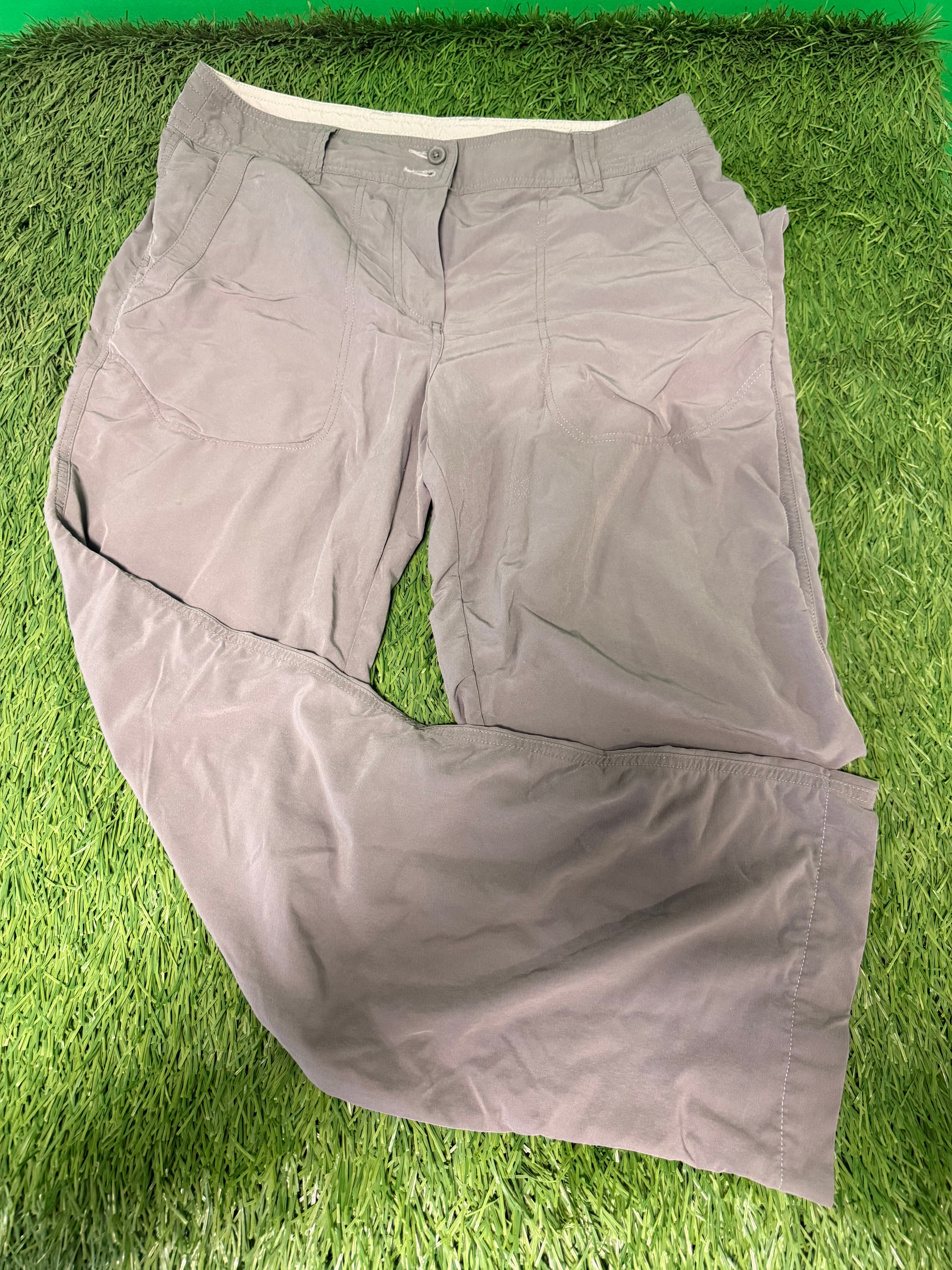 Beige casual lightweight trousers laid flat on green grass, showing front pockets and button closure