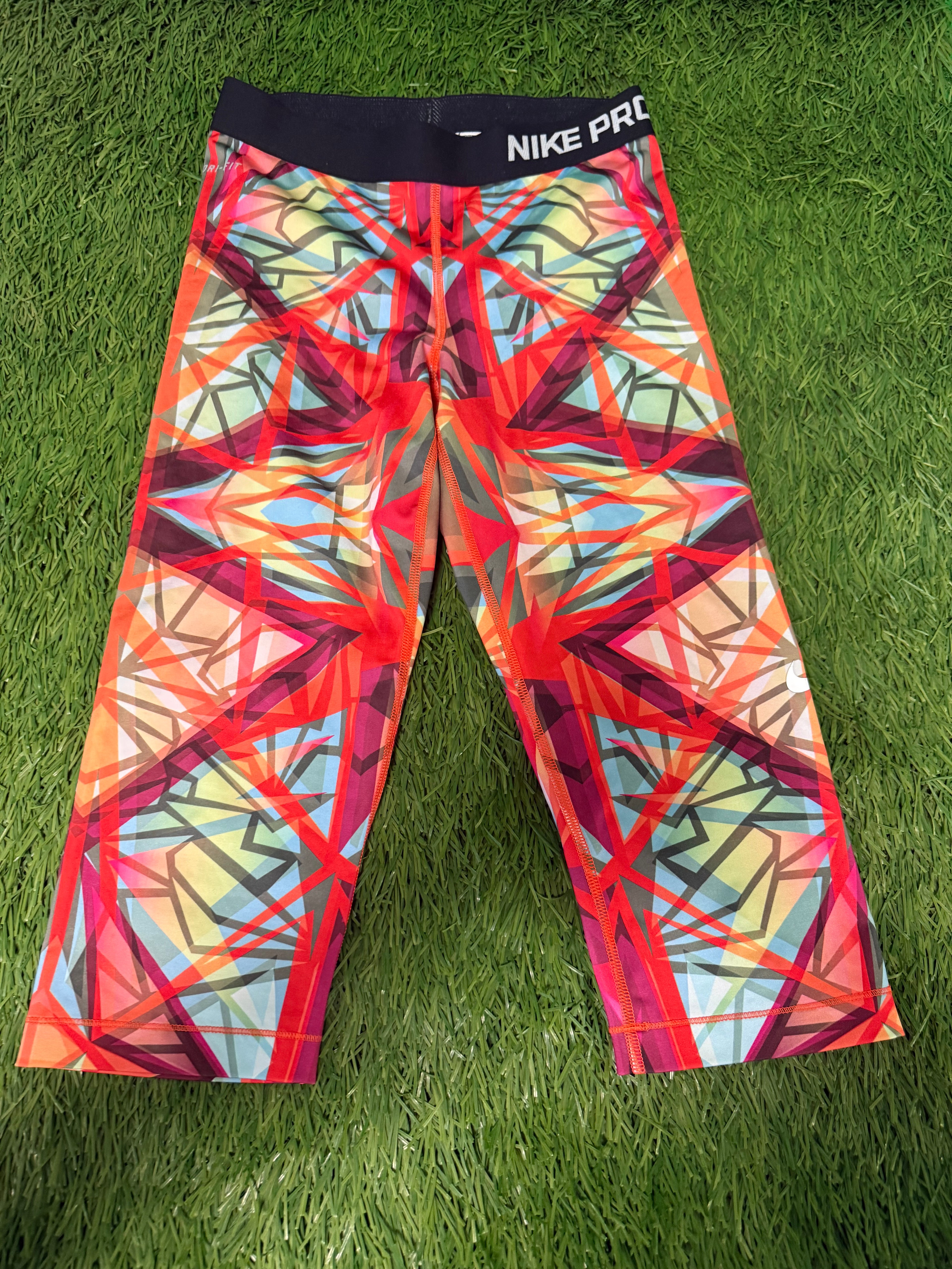 Nike Pro 3/4 length leggings with vibrant multicoloured geometric pattern laid flat on grass