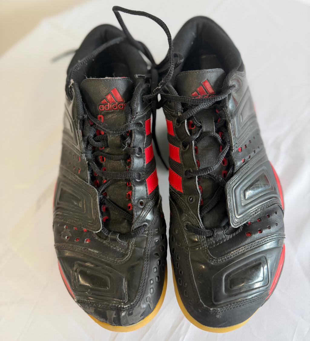 Pair of black and red Adidas indoor court shoes on white sheet