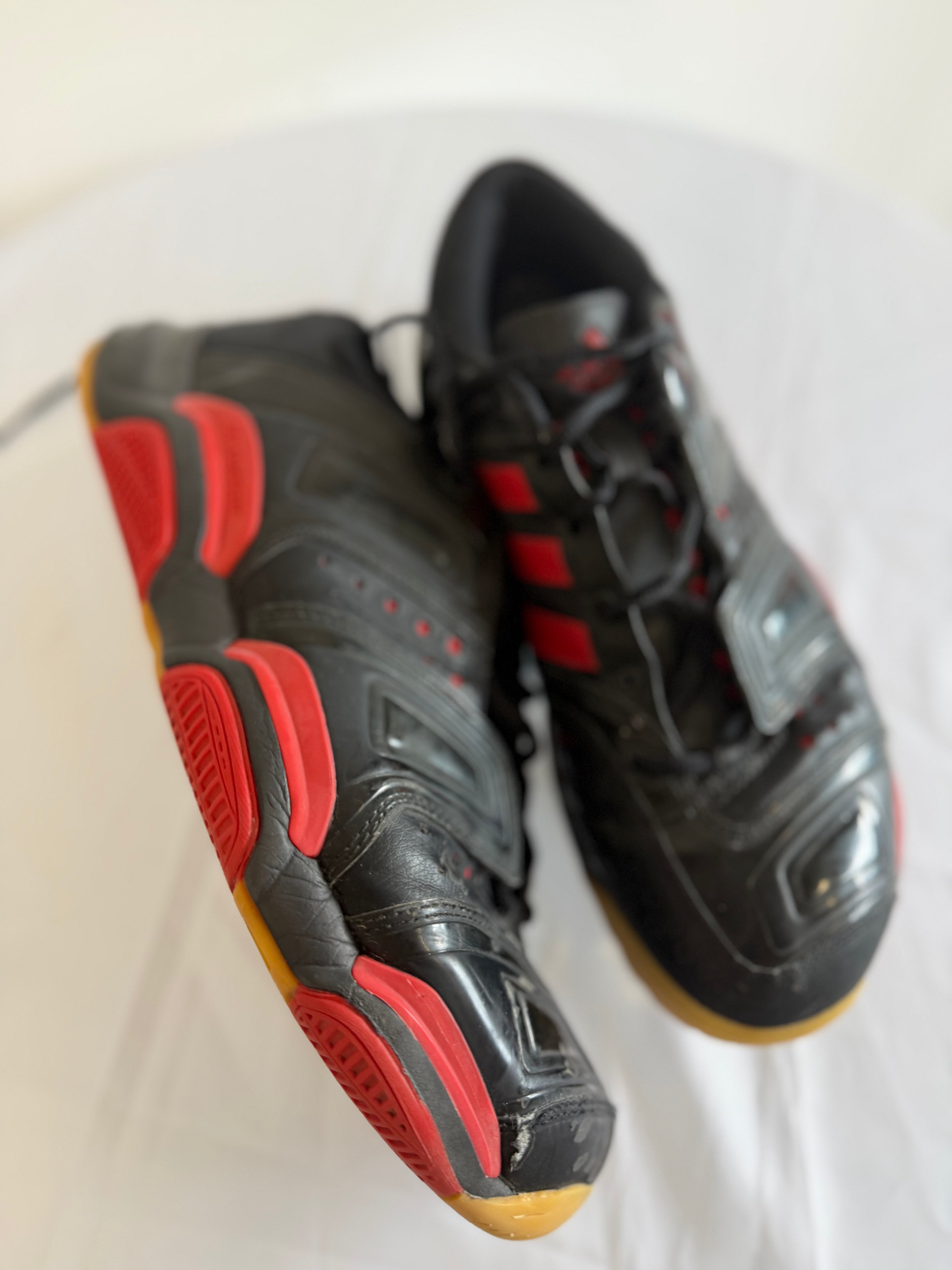 Side angle of Adidas black and red indoor court shoes, showing gum sole and details