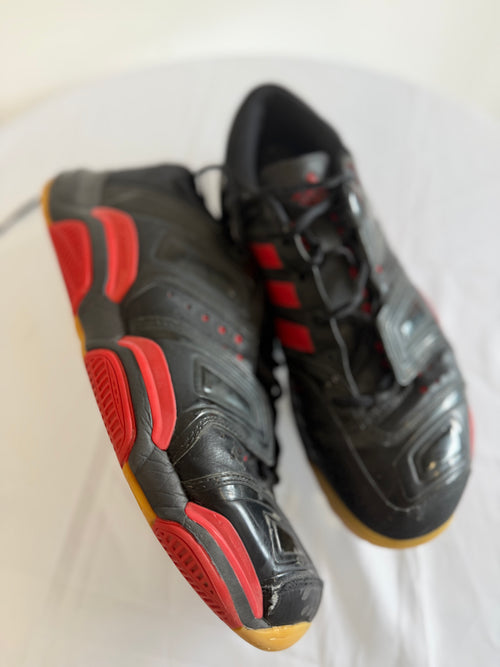 Side angle of Adidas black and red indoor court shoes, showing gum sole and details
