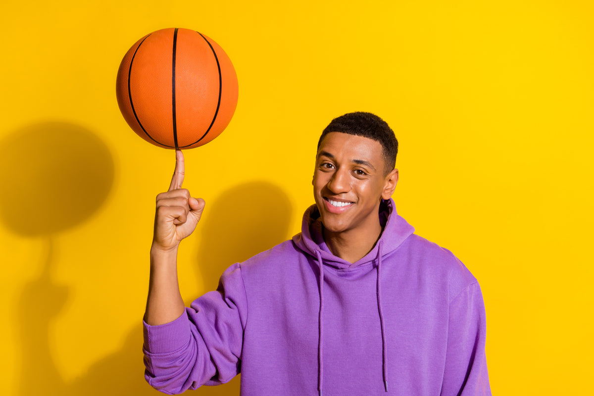 Person in a purple hoodie balancing a basketball on their finger against a yellow background