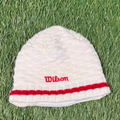 White knitted Wilson winter hat with red stripe and embroidered logo on green turf