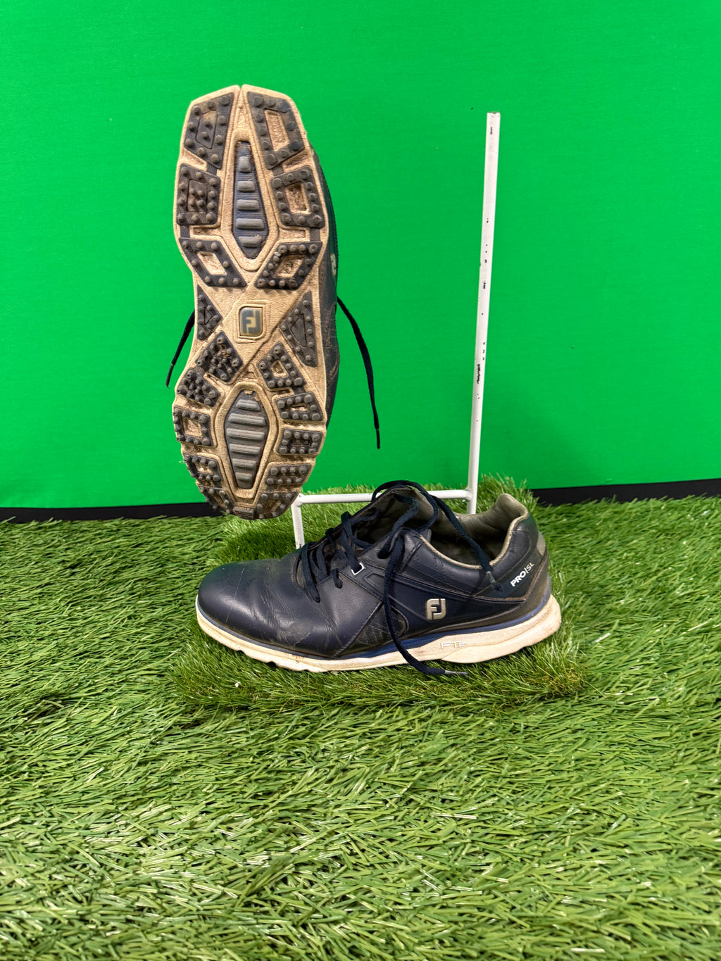 Right side view of black FootJoy Pro/SL golf shoe with visible textured sole and laces on artificial grass
