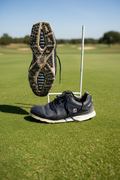 Right side view of black FootJoy Pro/SL golf shoe with visible textured sole and laces on artificial grass