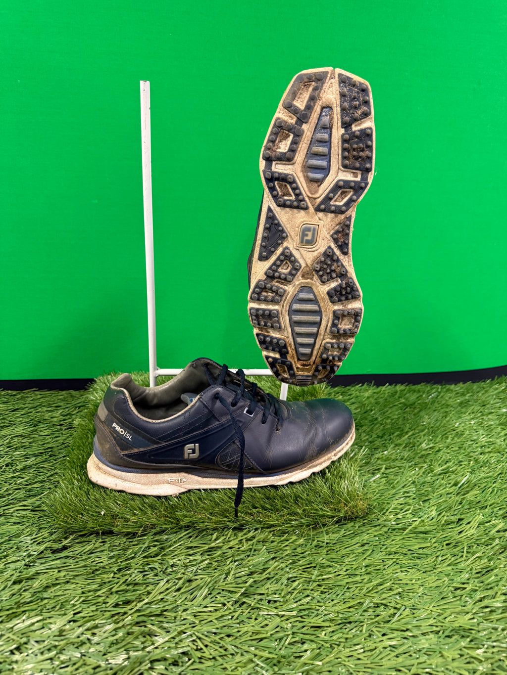 Left side view of black FootJoy Pro/SL golf shoe showing detailed tread pattern and construction on artificial grass