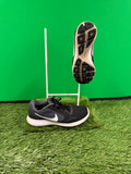 Black and grey Nike running trainers on green artificial grass with one shoe sole facing forward highlighting traction pattern