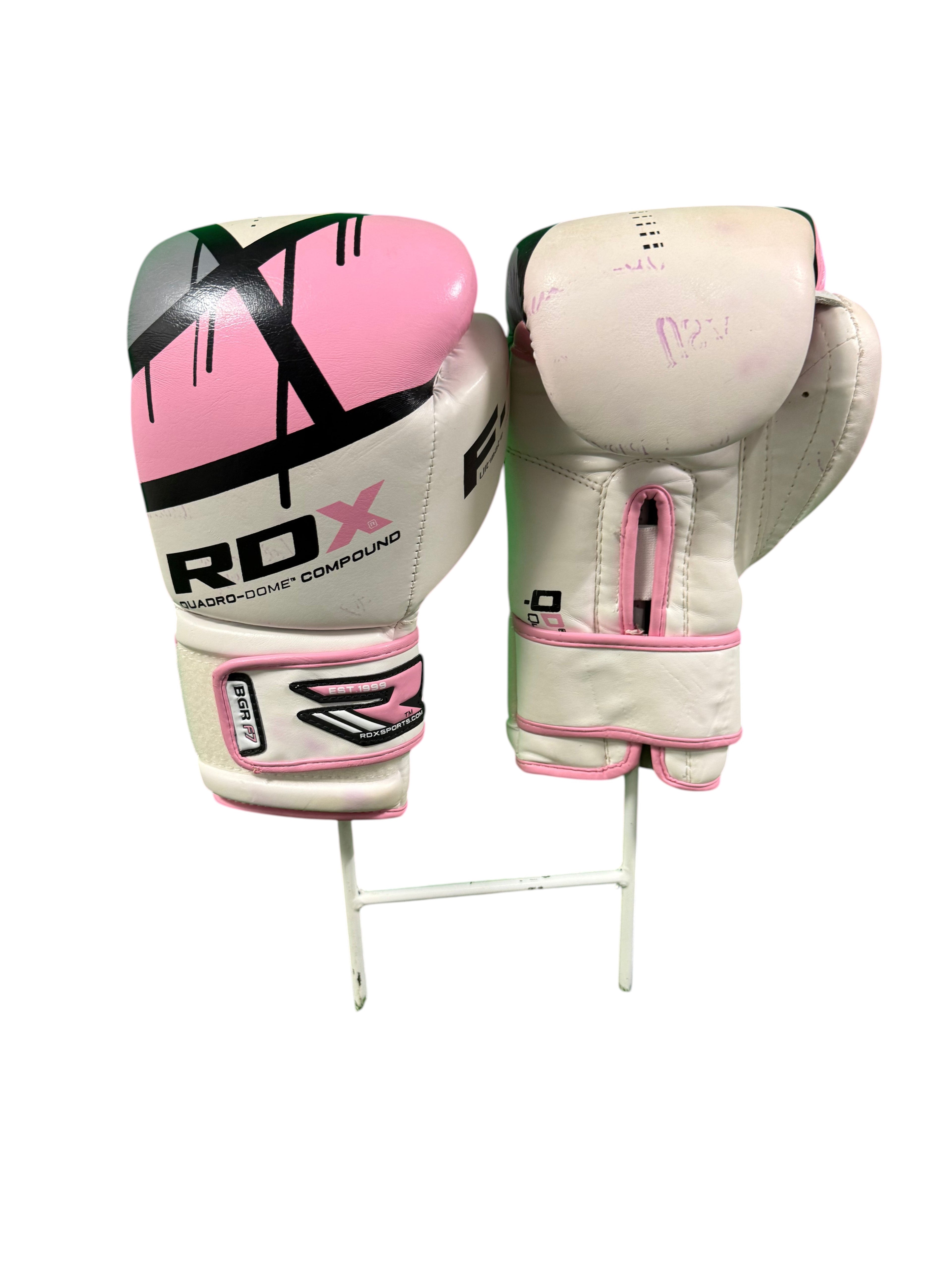 Pair of white and pink RDX boxing gloves displayed on a stand against a green background