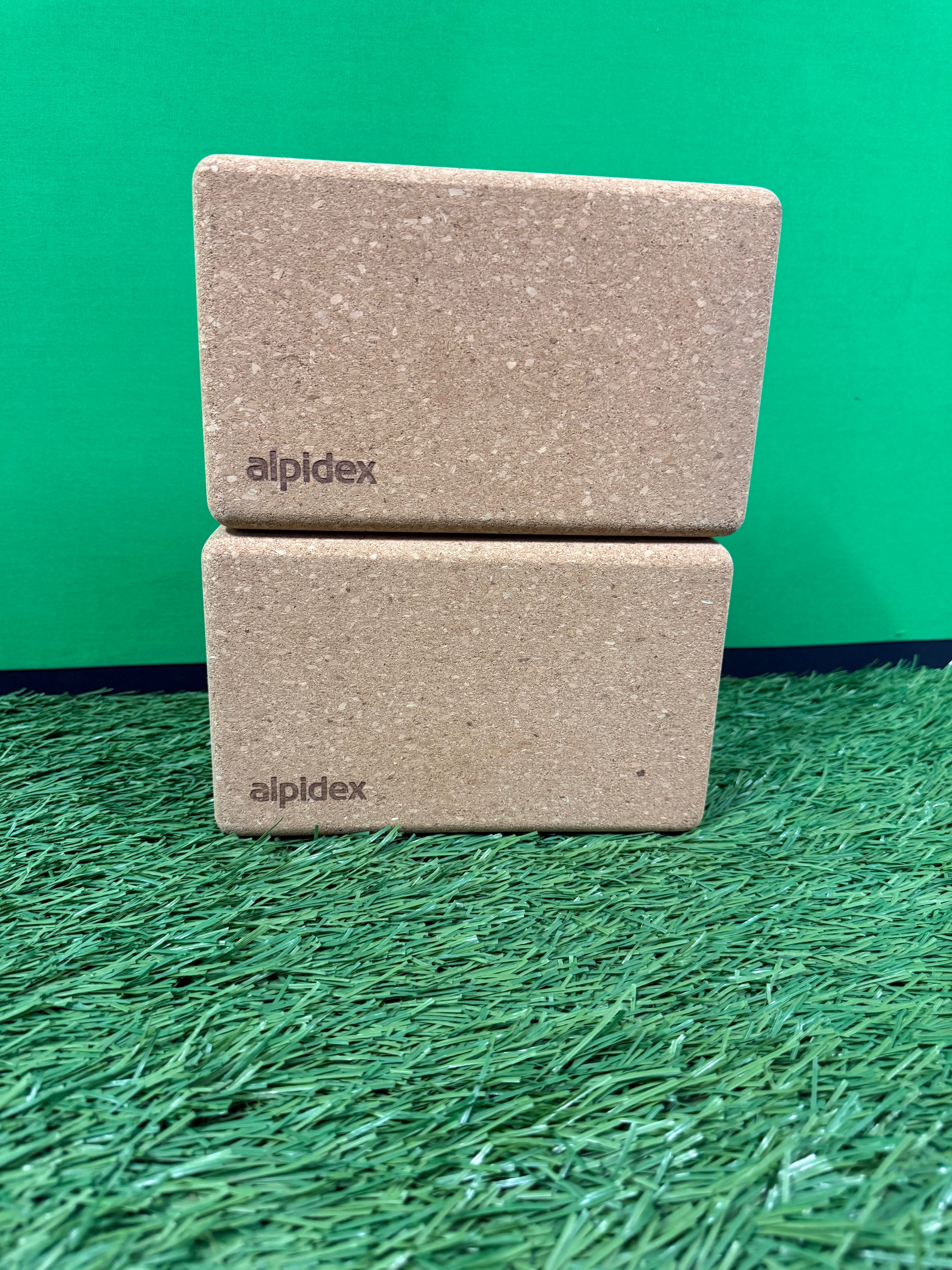 Two natural cork yoga blocks stacked on green artificial grass with green background
