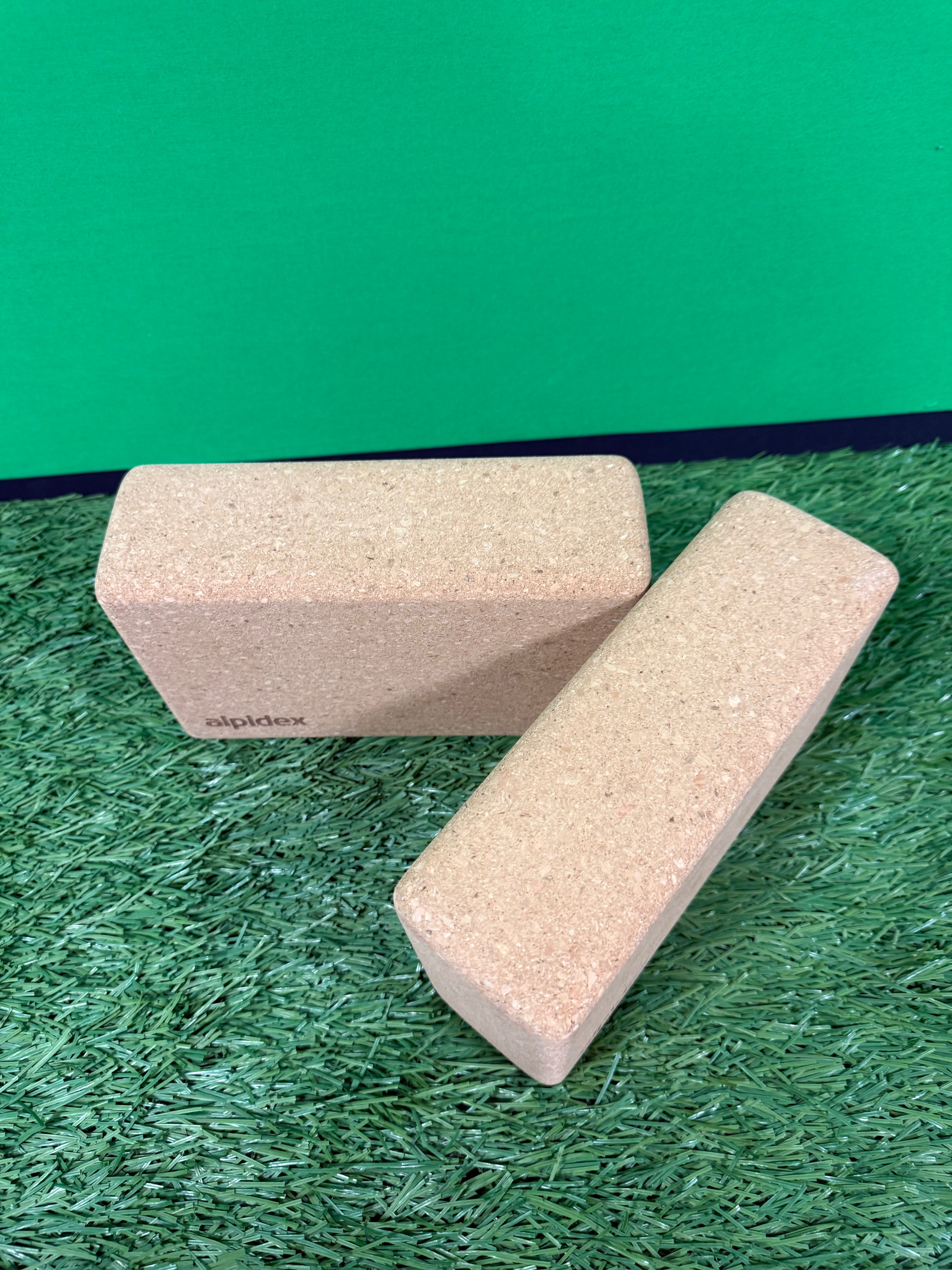 Two cork yoga blocks positioned at angles on artificial grass against a green background