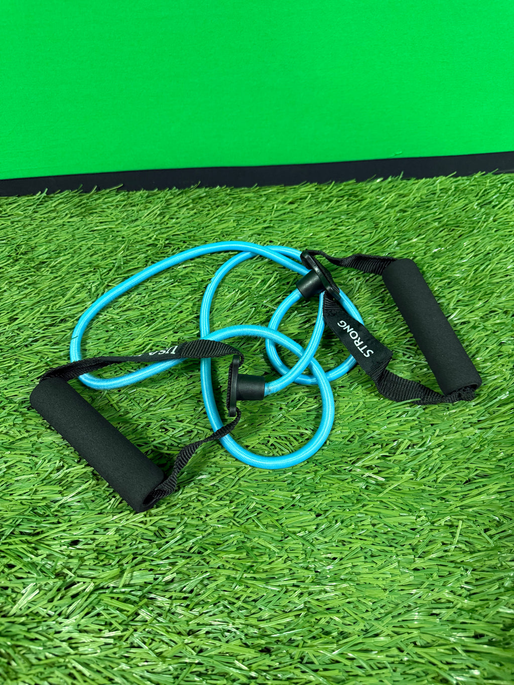 Blue resistance band with black foam handles lying on artificial grass