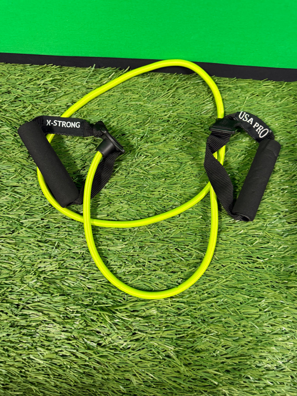 Neon yellow resistance band with black foam handles lying on artificial grass