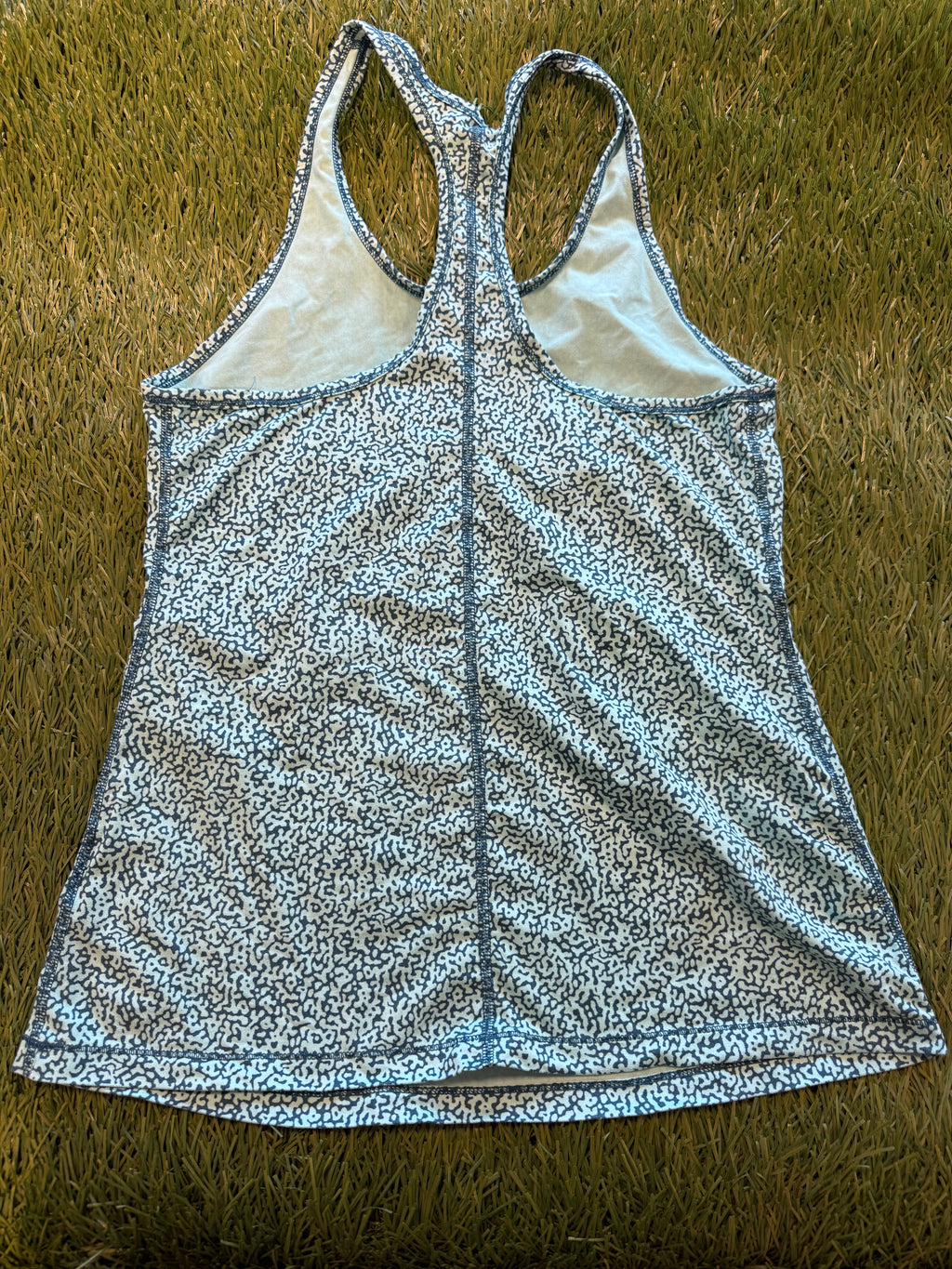 Back view of Nike women's racerback tank top with blue and white abstract pattern, showing racerback cut and detailed stitching, laid flat on grass.