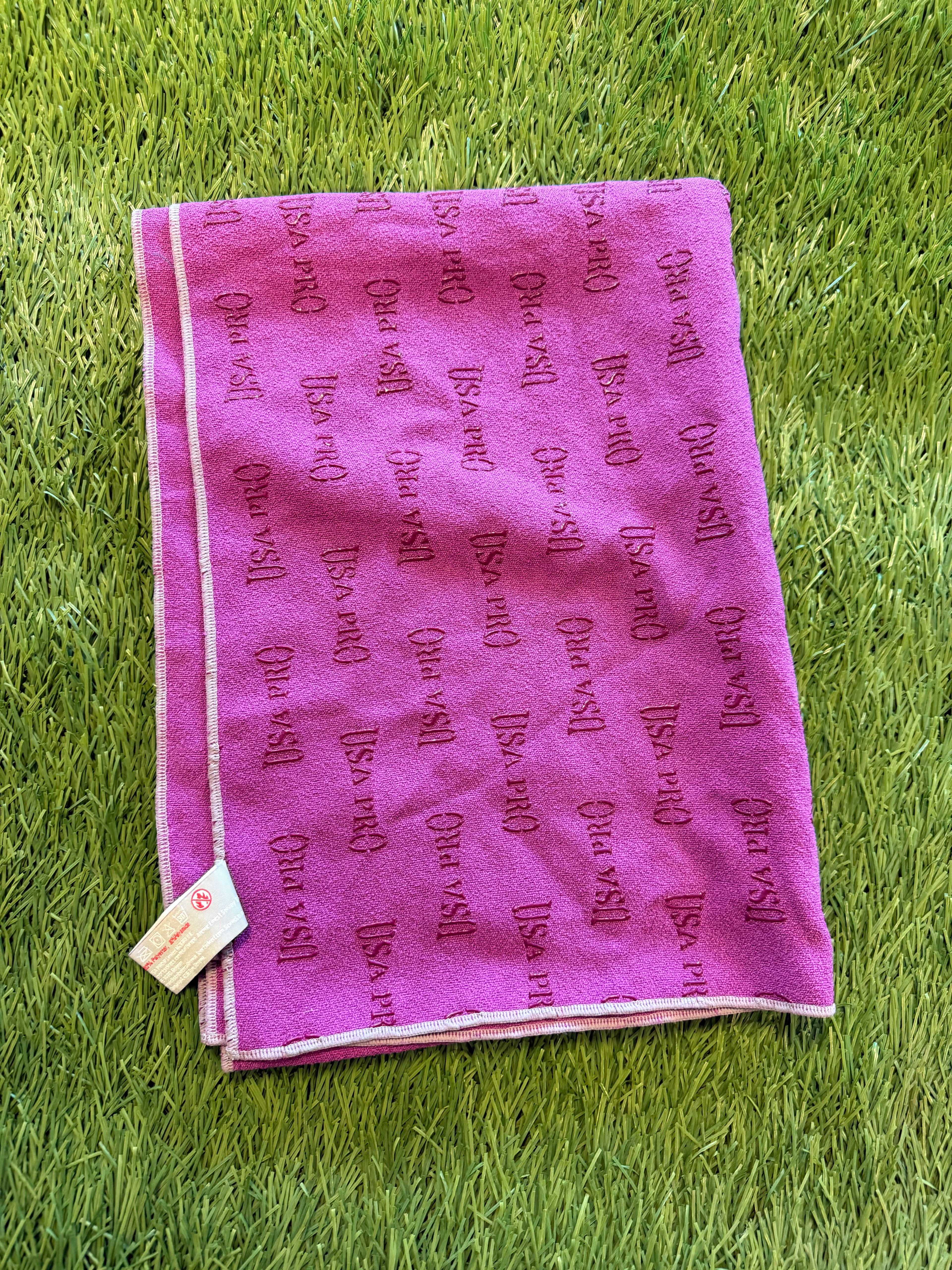 Folded purple USA Pro microfiber sports towel with embossed logo pattern on green grass background