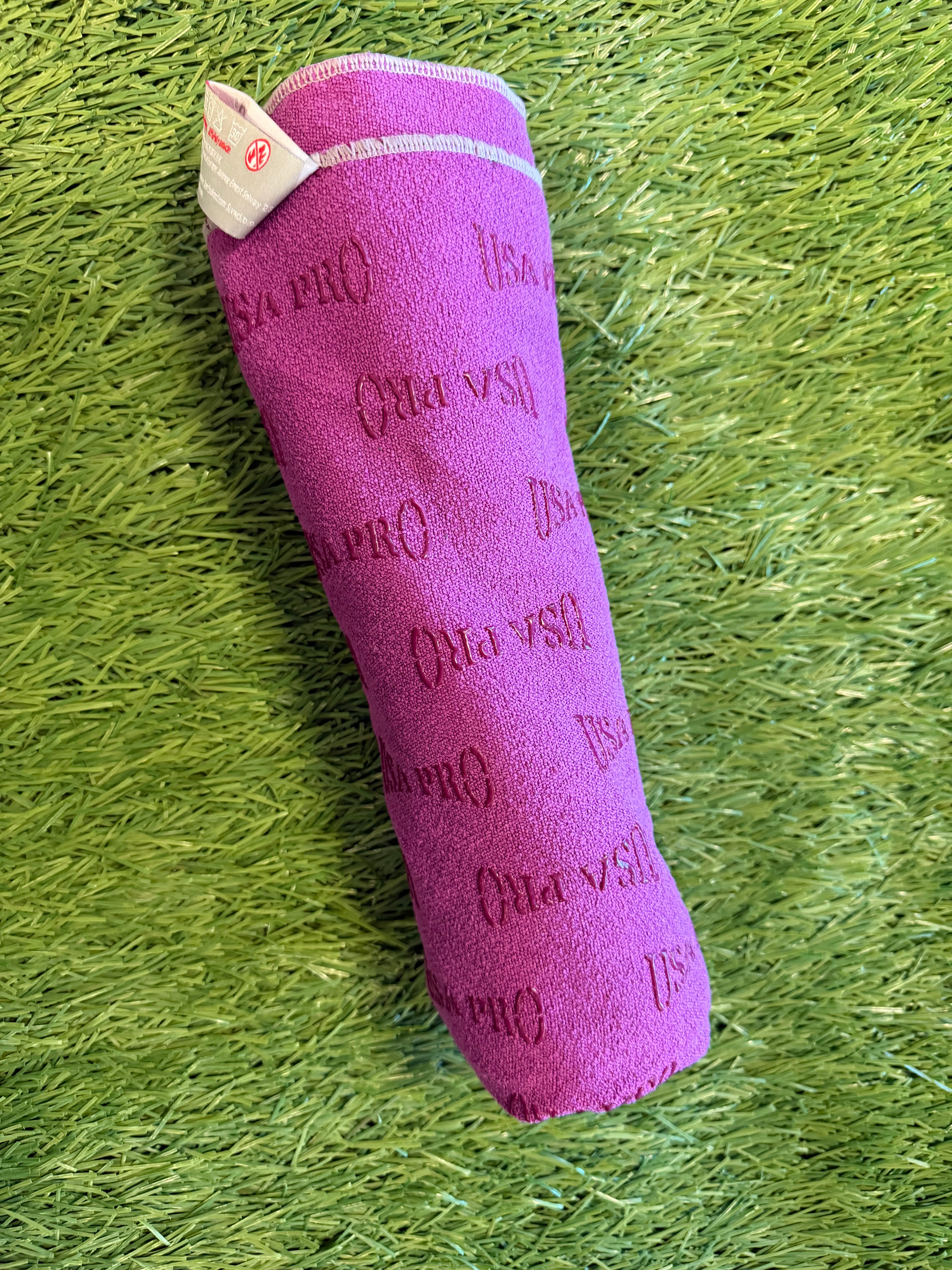 Rolled purple USA Pro microfiber sports towel showing textured logo embossing and stitched edges on green grass