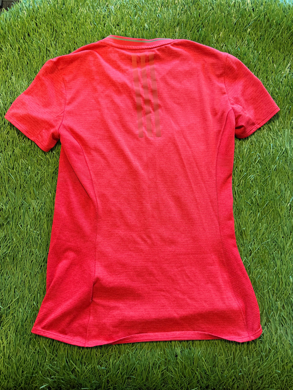 Back view of the same red Adidas Supernova women's running t-shirt on grass displaying subtle mesh side panels and three vertical stripes on upper back