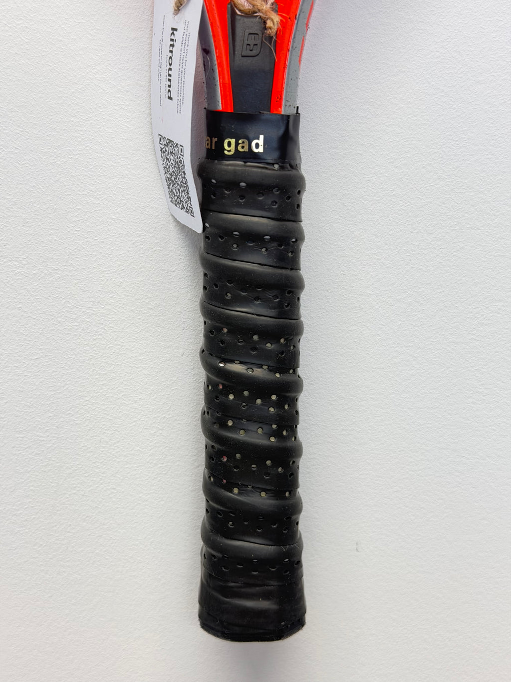 Close-up of black perforated grip on red tennis racket