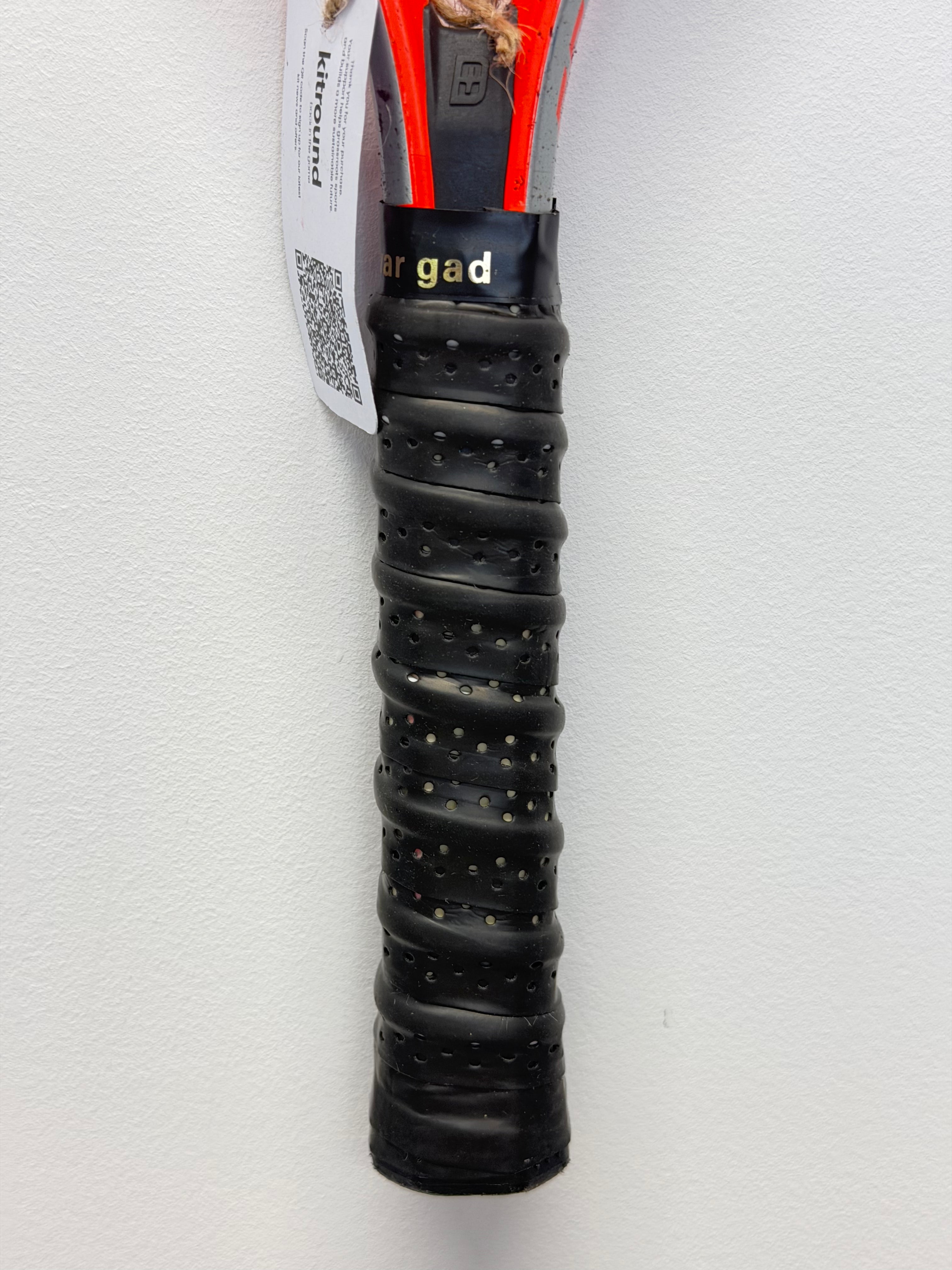 Close-up of black perforated grip on red tennis racket