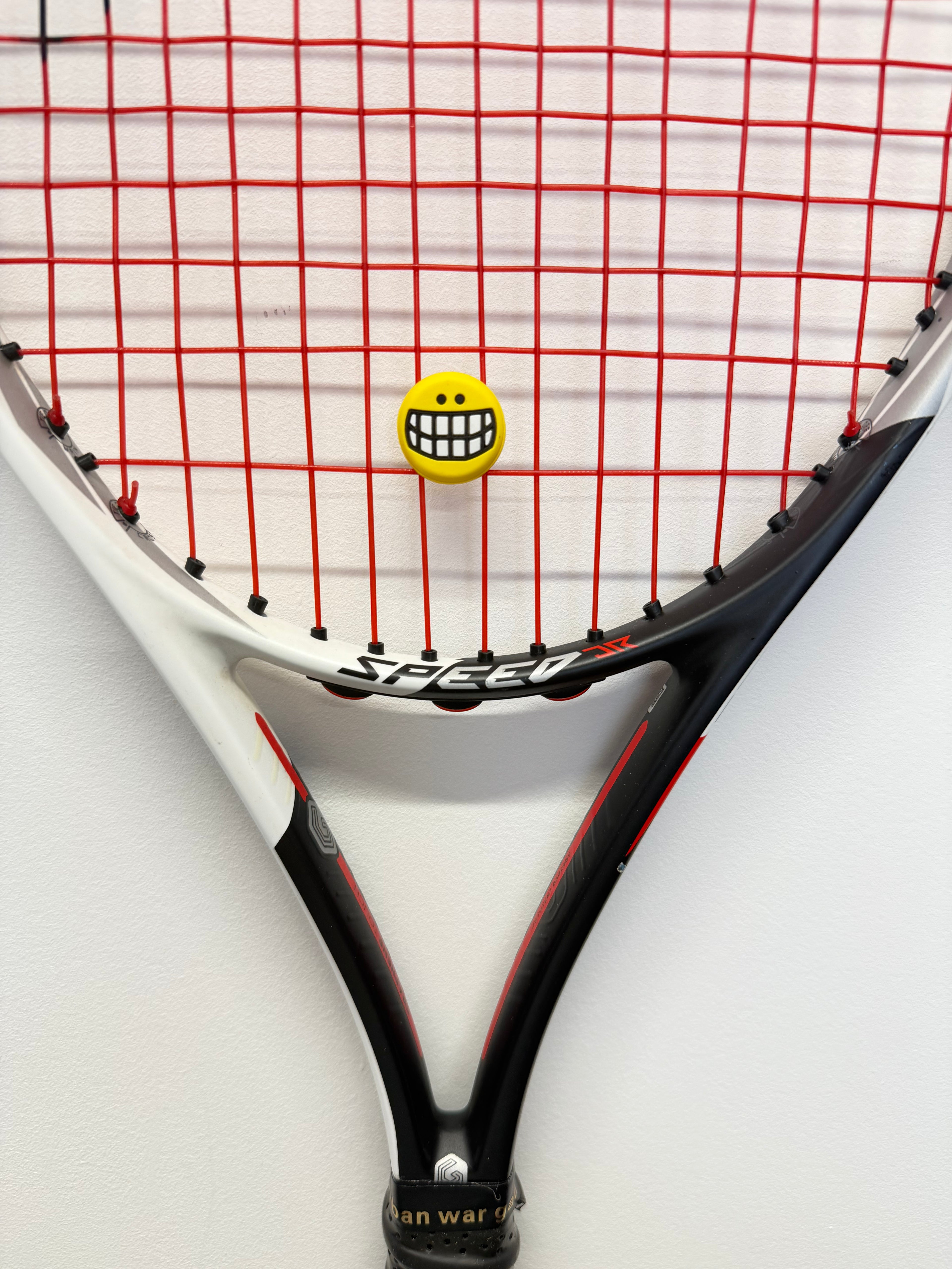 Head Speed Junior Tennis Racket with red strings and smiley face vibration dampener