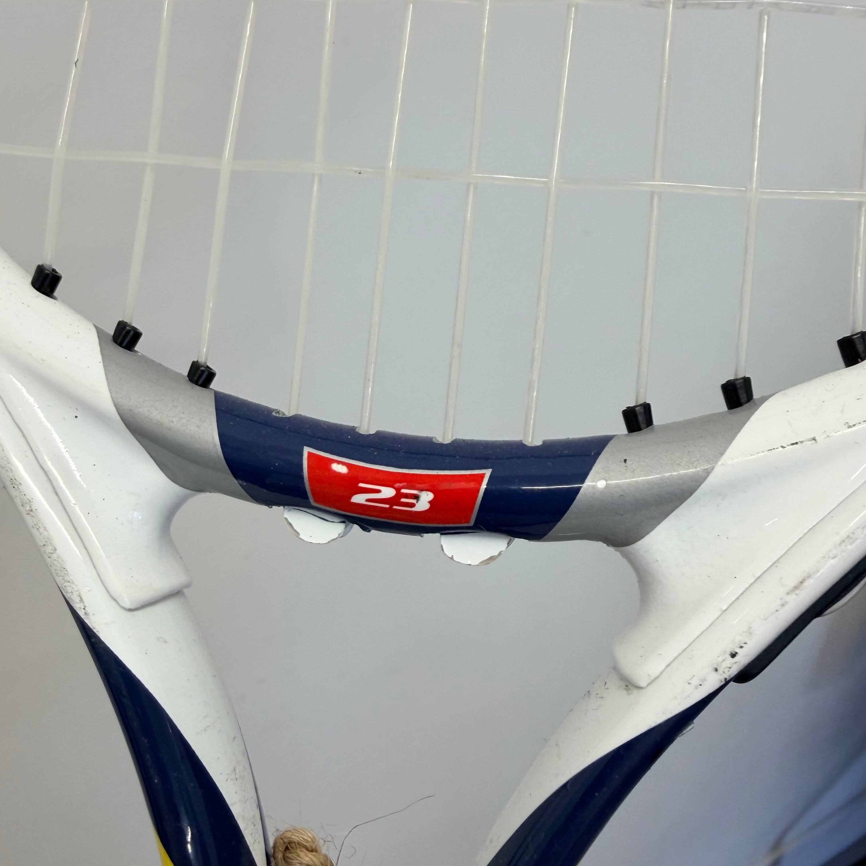 Close up of the throat and strings on a Wilson Steam 23 inch tennis racket in white, blue, yellow, and red