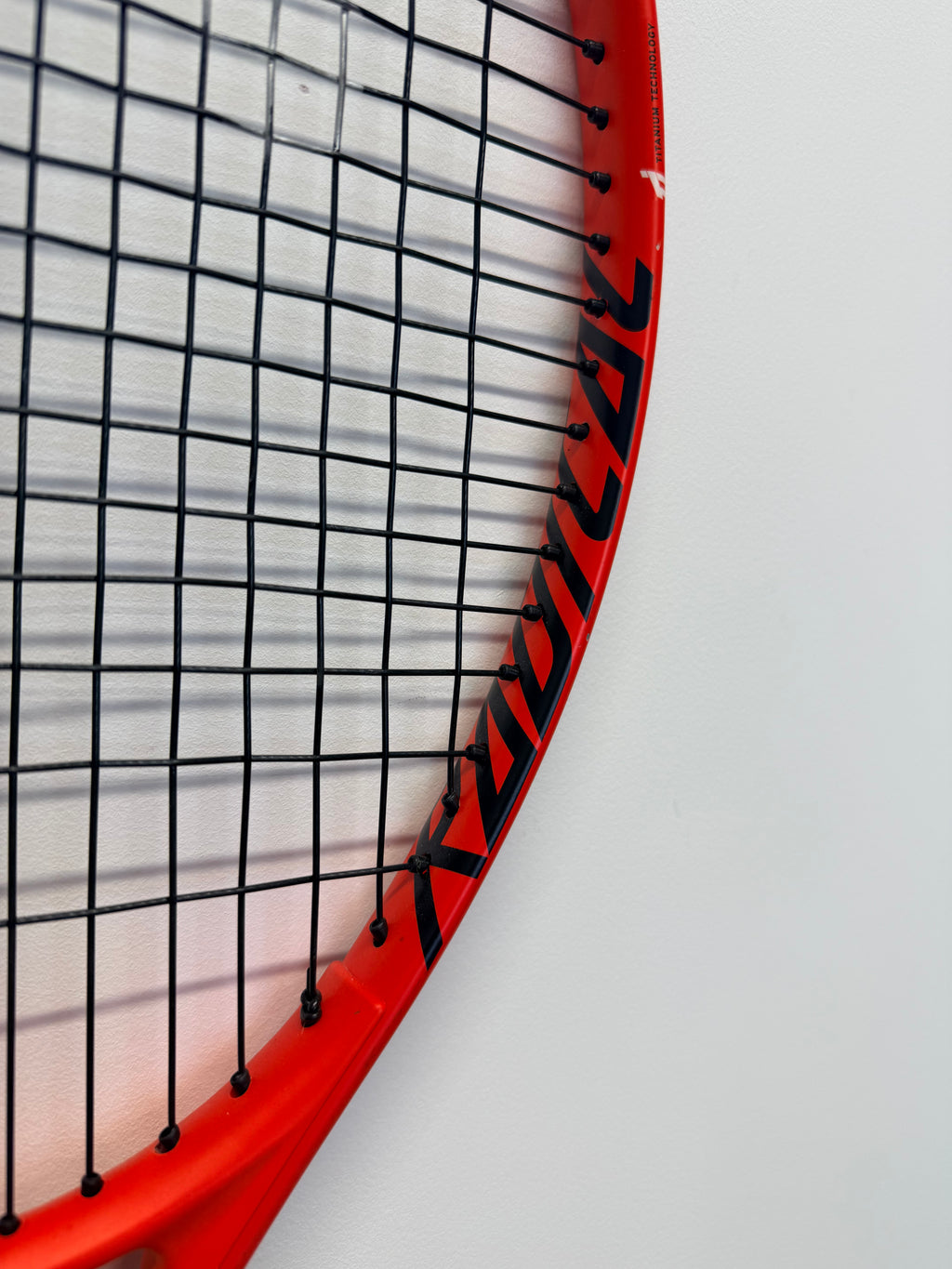 Side angle of Head Radical 27 tennis racket head highlighting strings and branding
