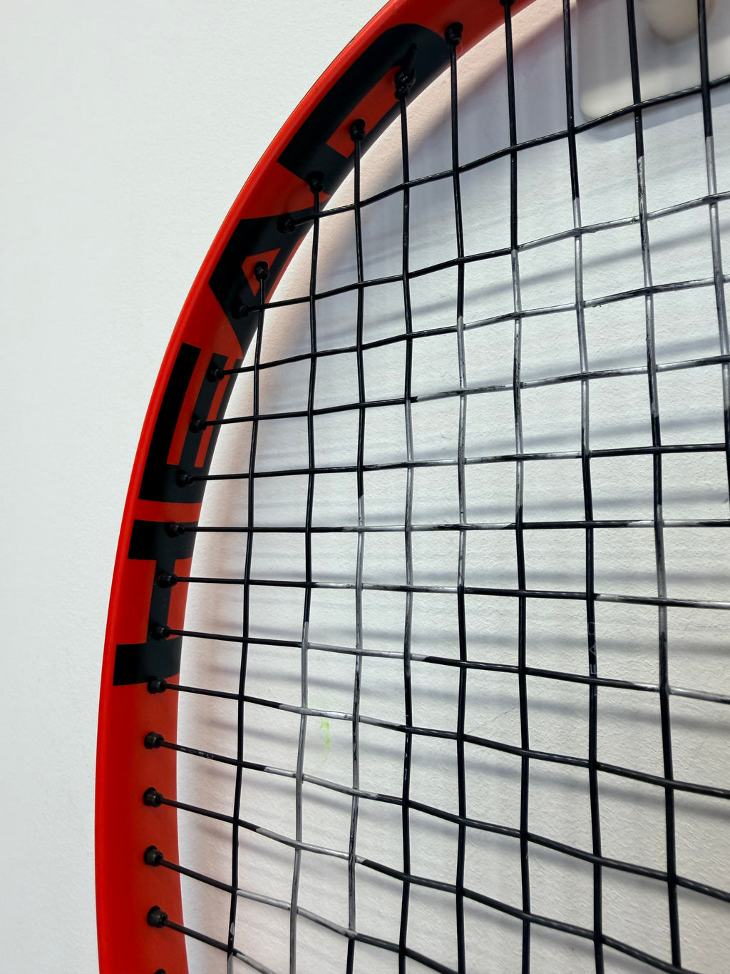 Partial view of tennis racket head with black string pattern and red frame