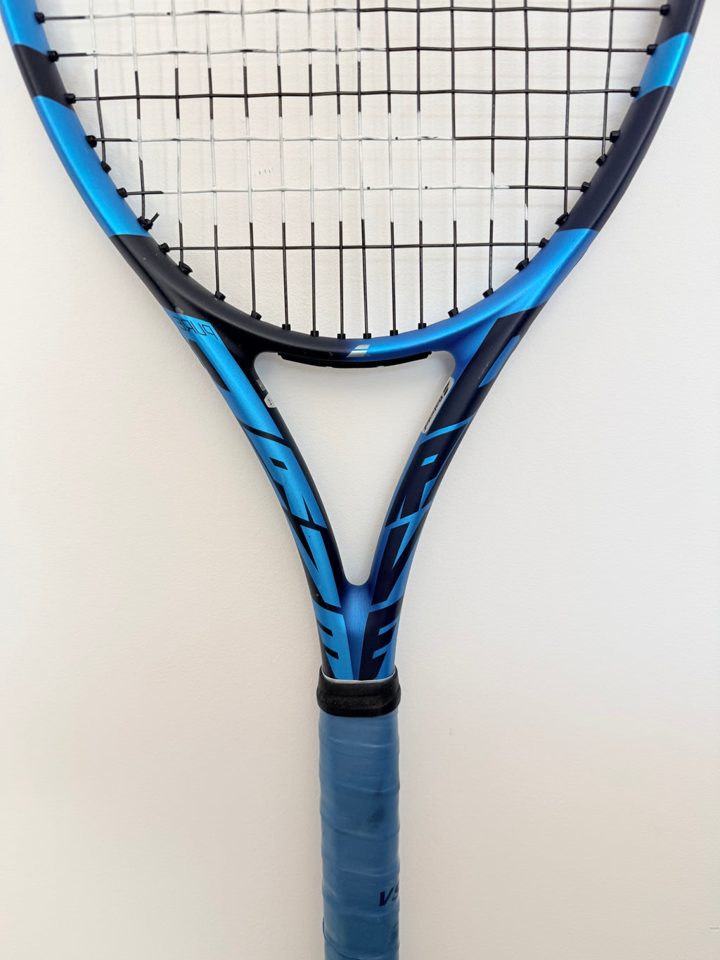 Partial view of Babolat blue tennis racket with black grip and strings