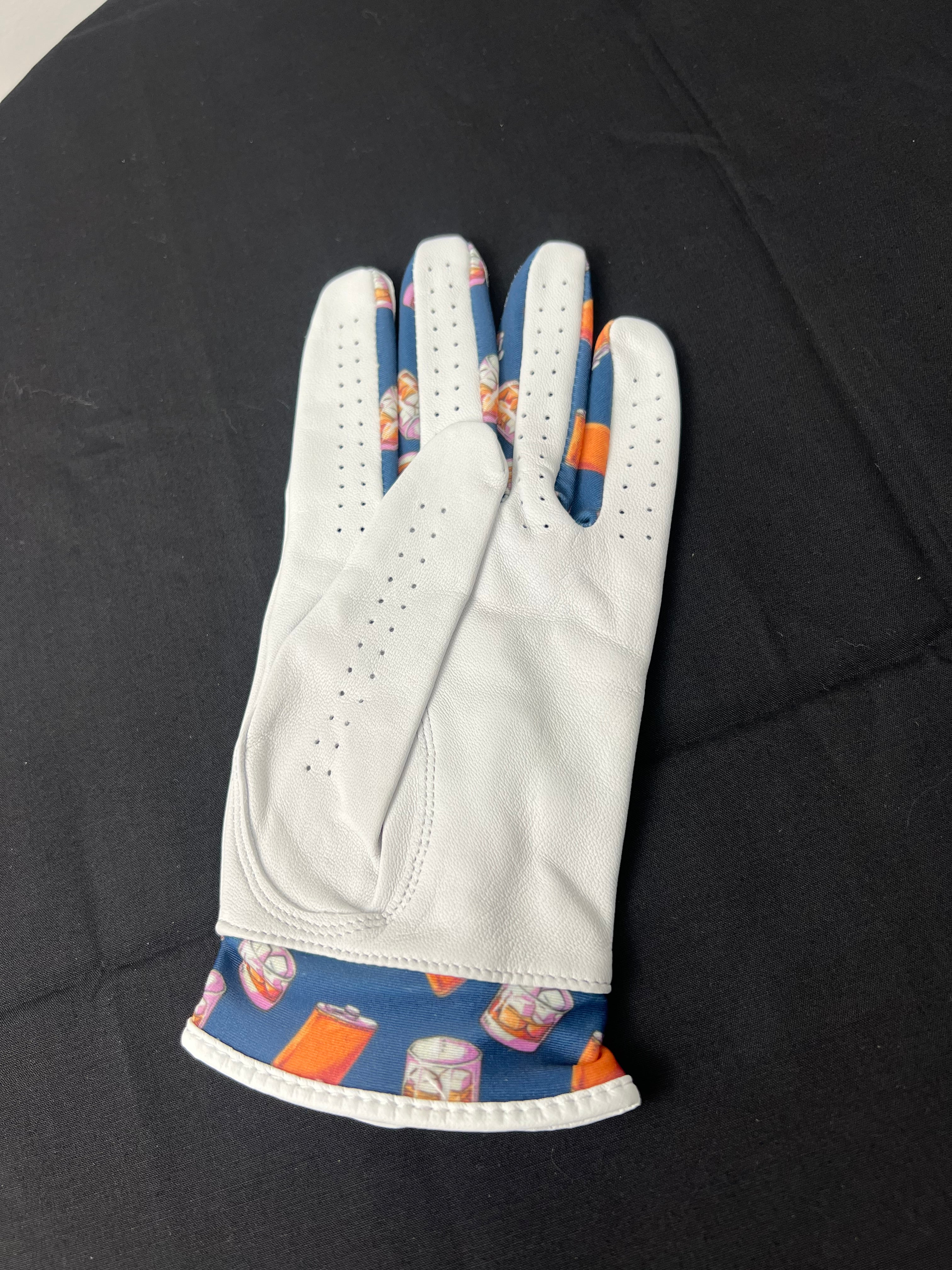 Backside of women's white golf glove with whiskey motif cuff, left hand, on black surface