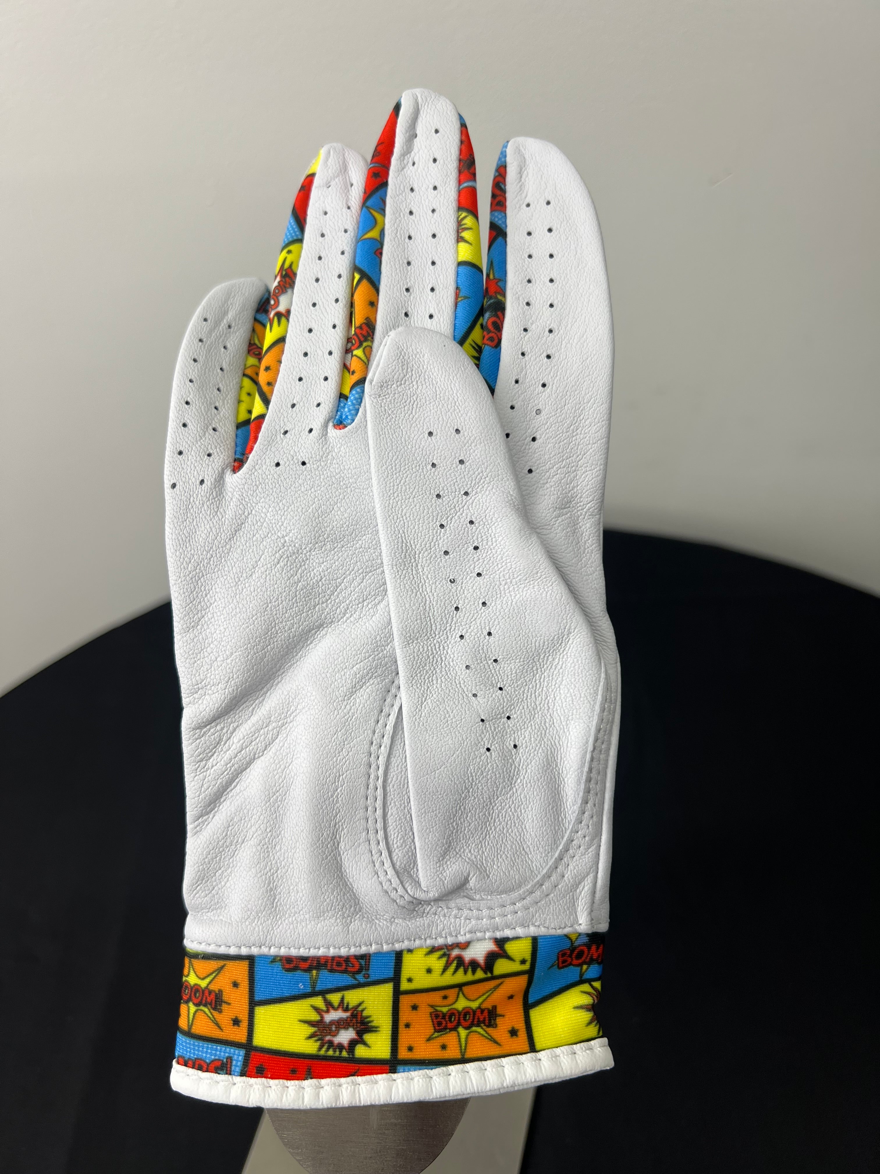 Back view of women's white golf glove featuring comic book style design details in red, yellow, and blue