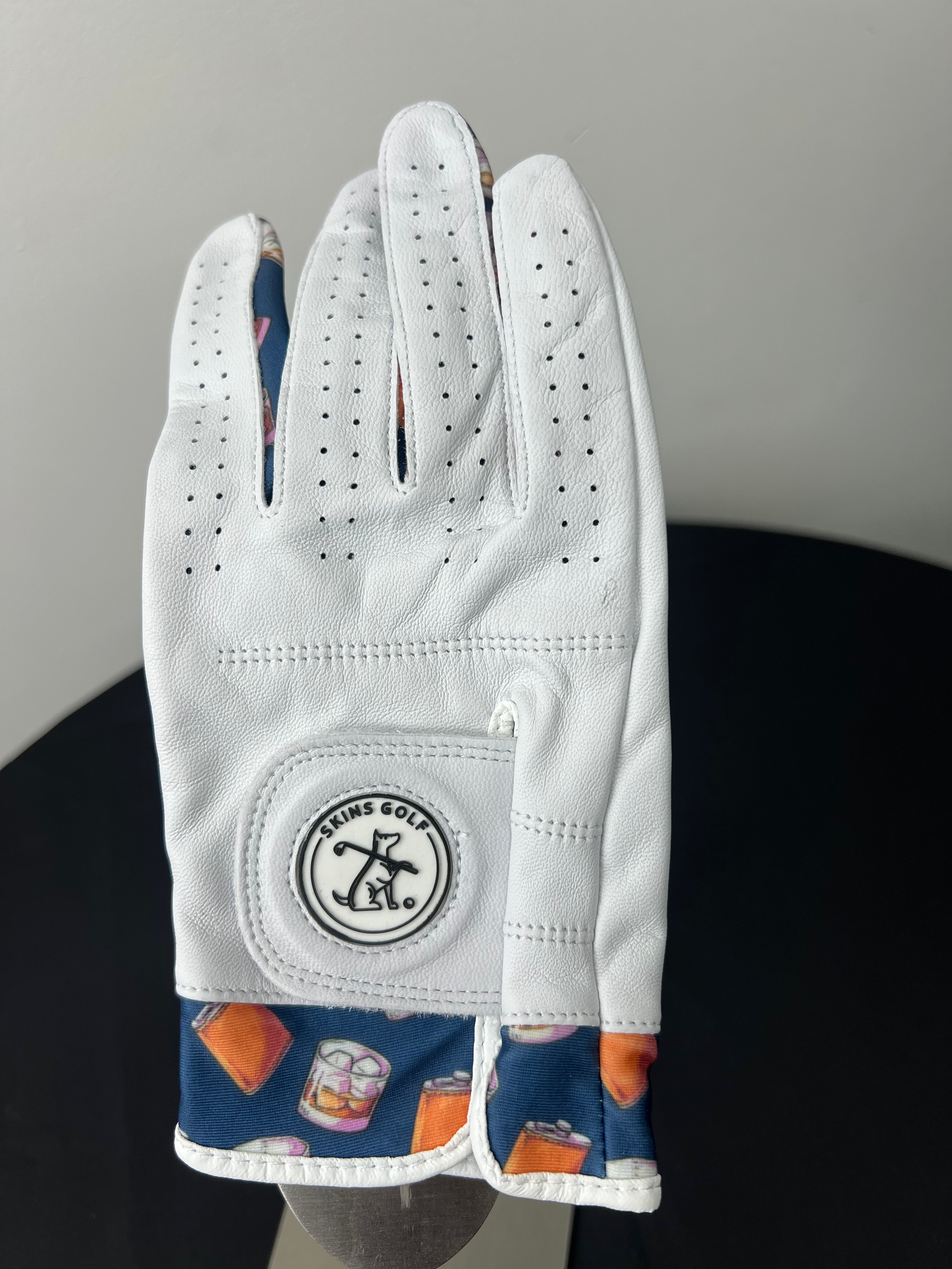 Front view of a women's white Skins Golf glove with whiskey and flask pattern on edge