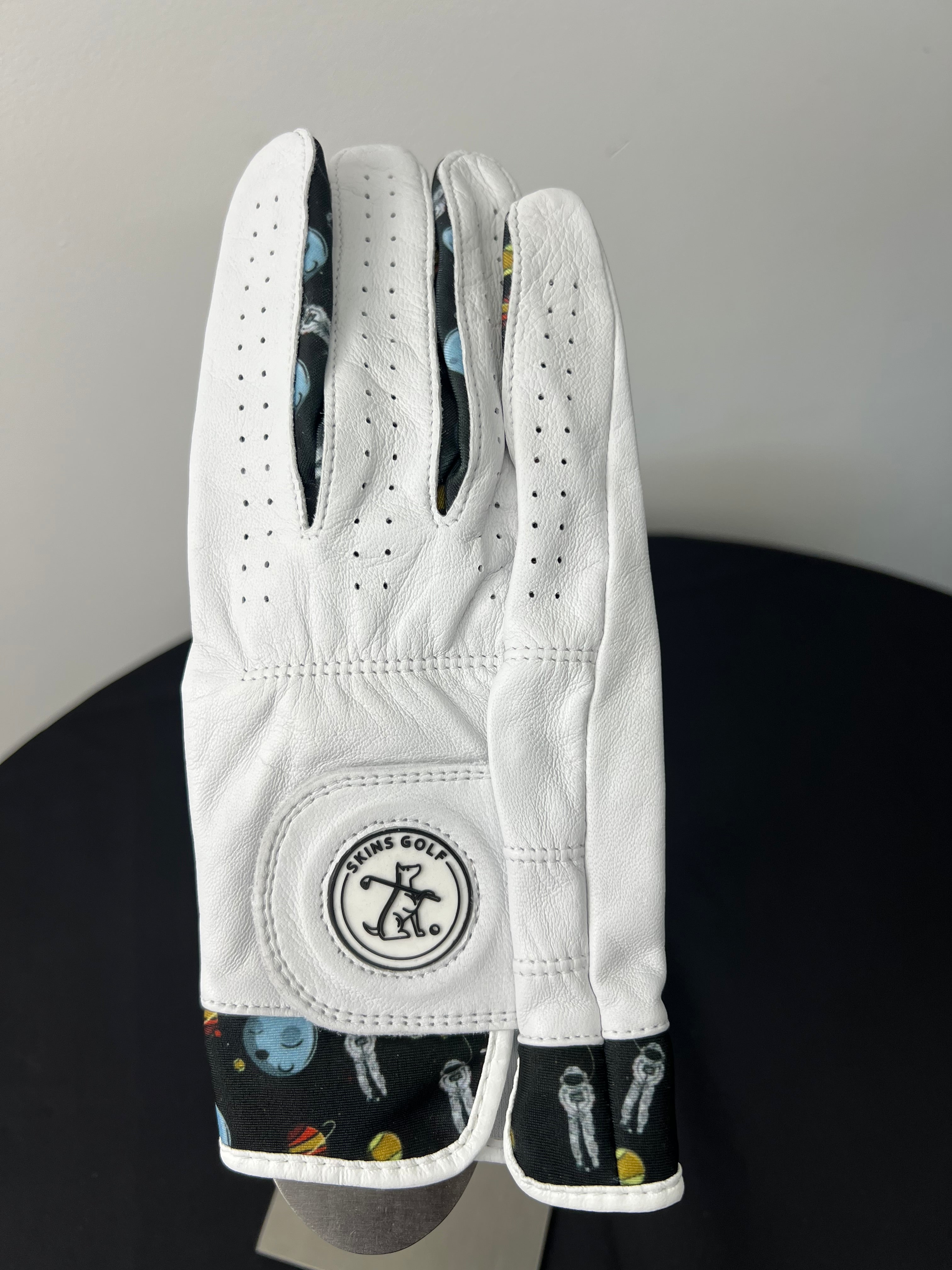 White women's golf glove with space-themed motif and Skins Golf logo displayed on the closure