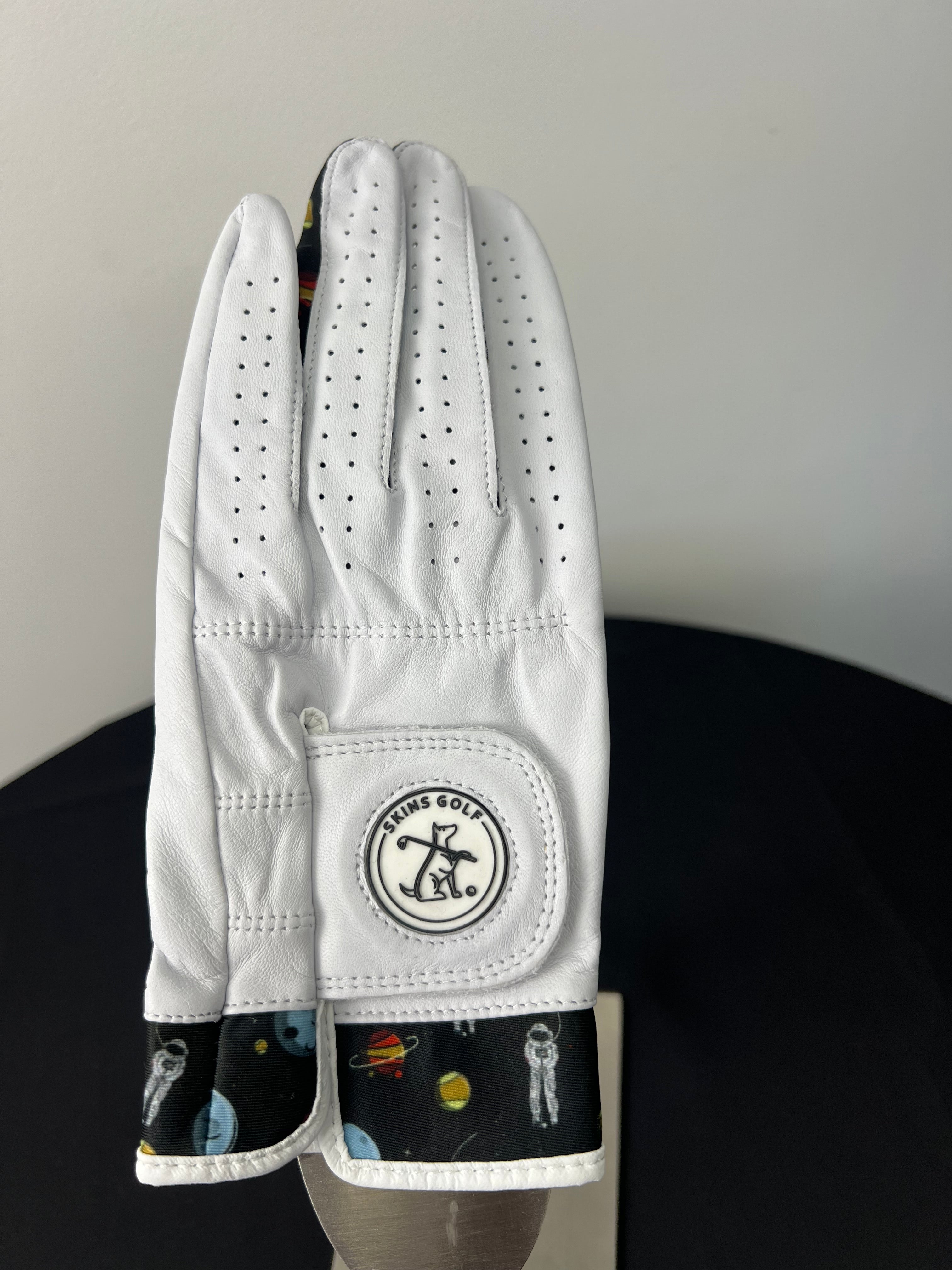 White golf glove with space motif trim and Skins Golf logo, shown palm side up