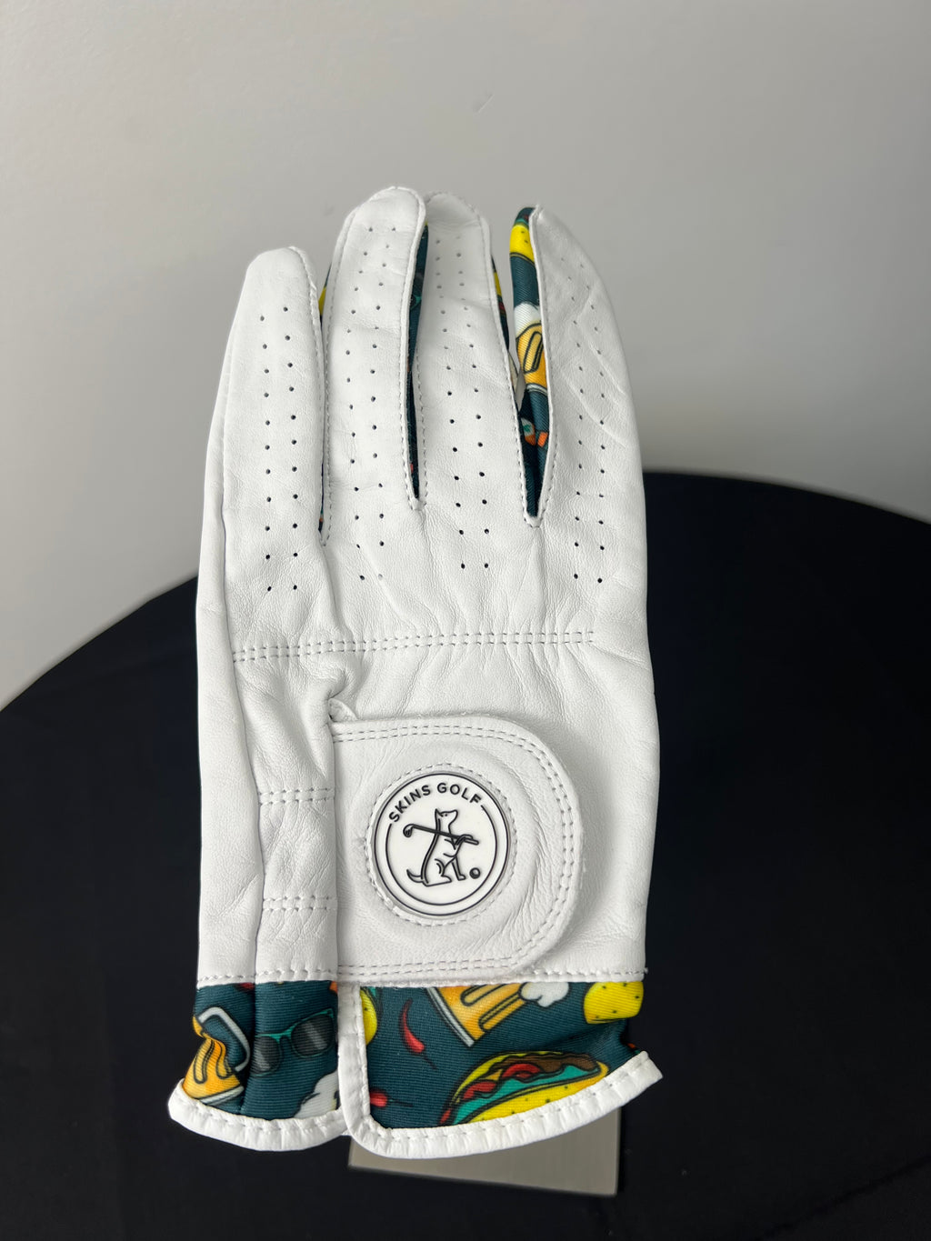 Women's white golf glove with colorful taco motif and Skins Golf logo on a black surface