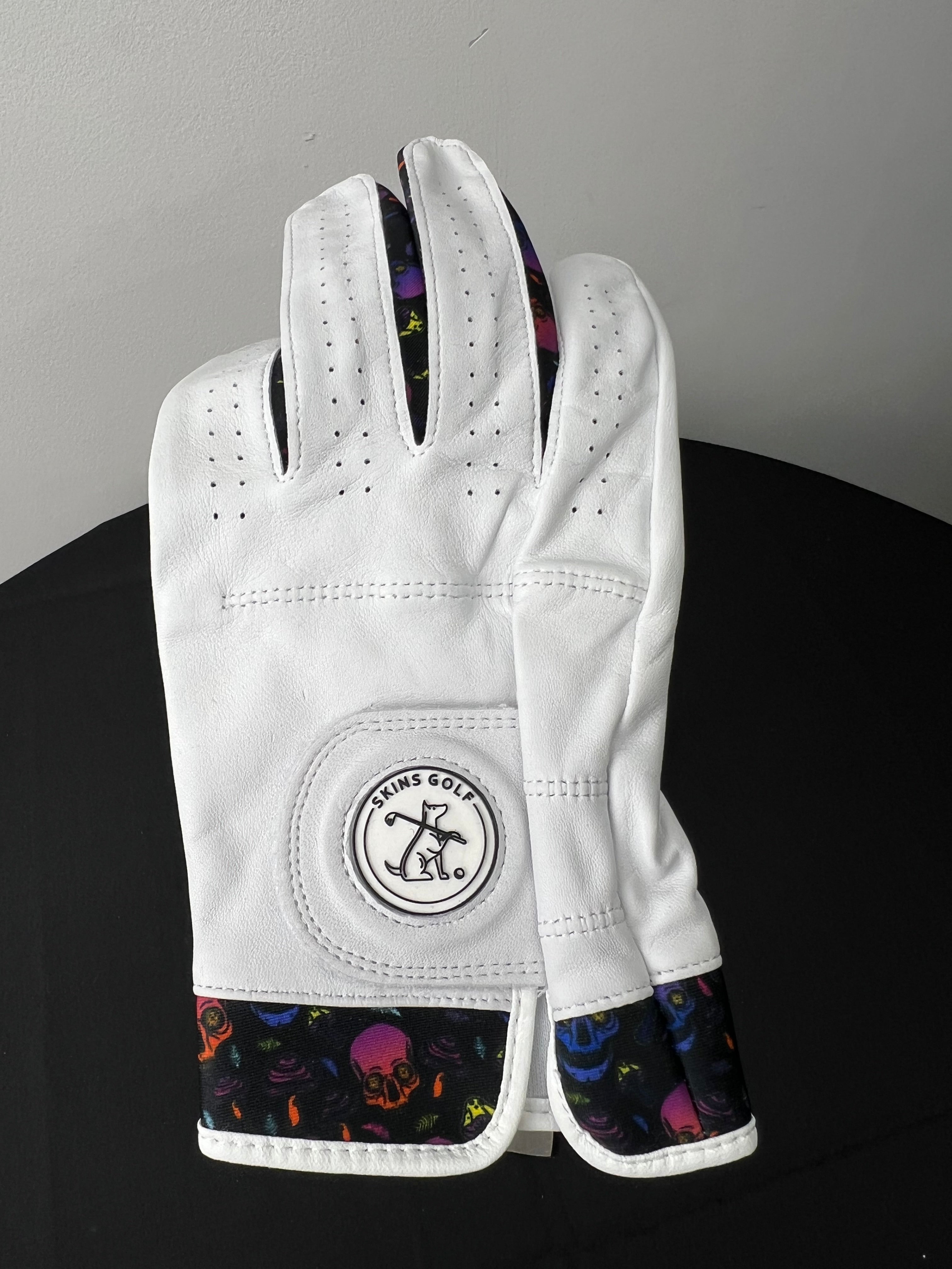 White golf glove with colorful skulls motif on cuff and between fingers, Skins Golf logo