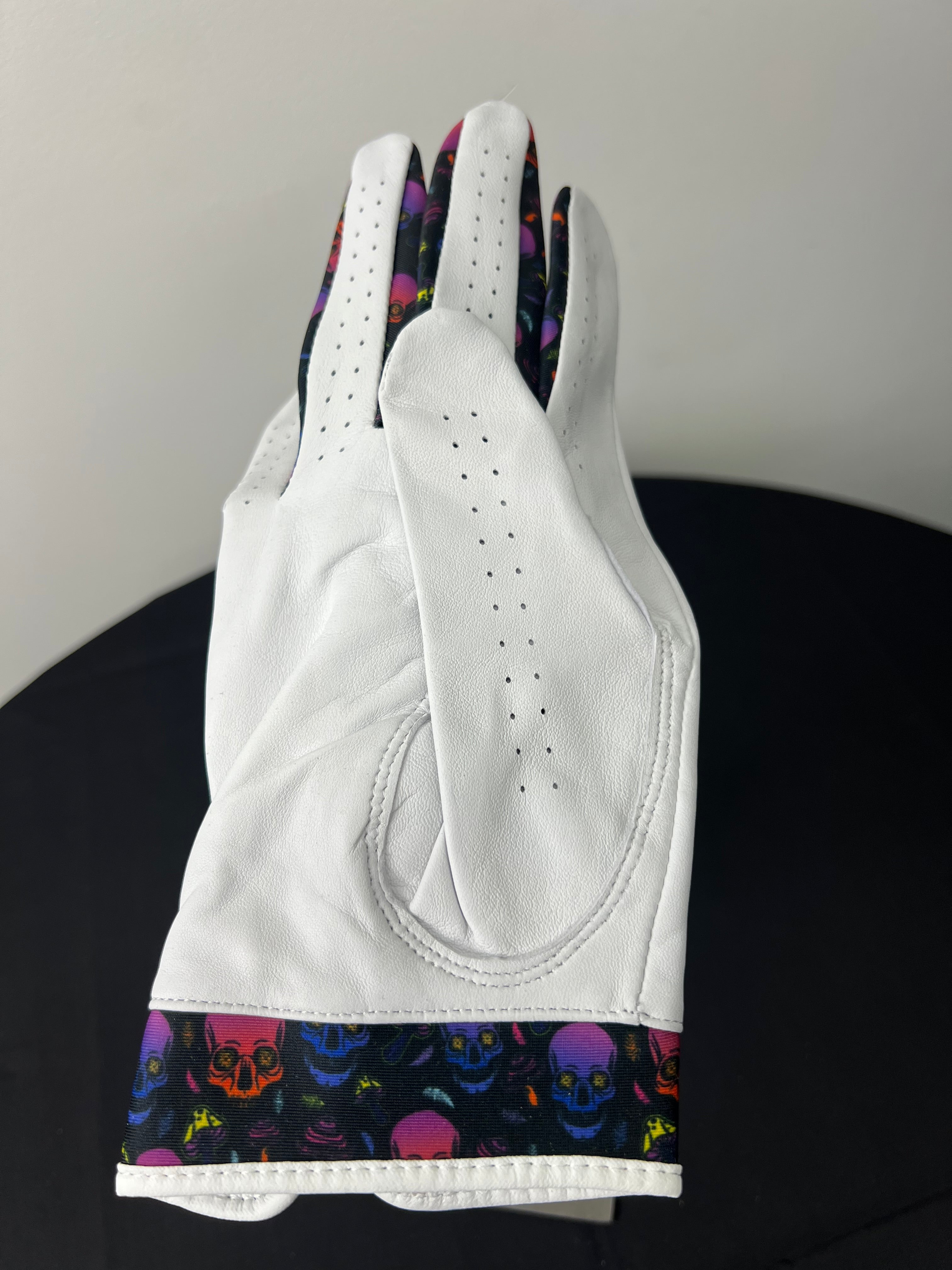 Back view of white golf glove featuring vibrant skulls motif trim and detailed stitching