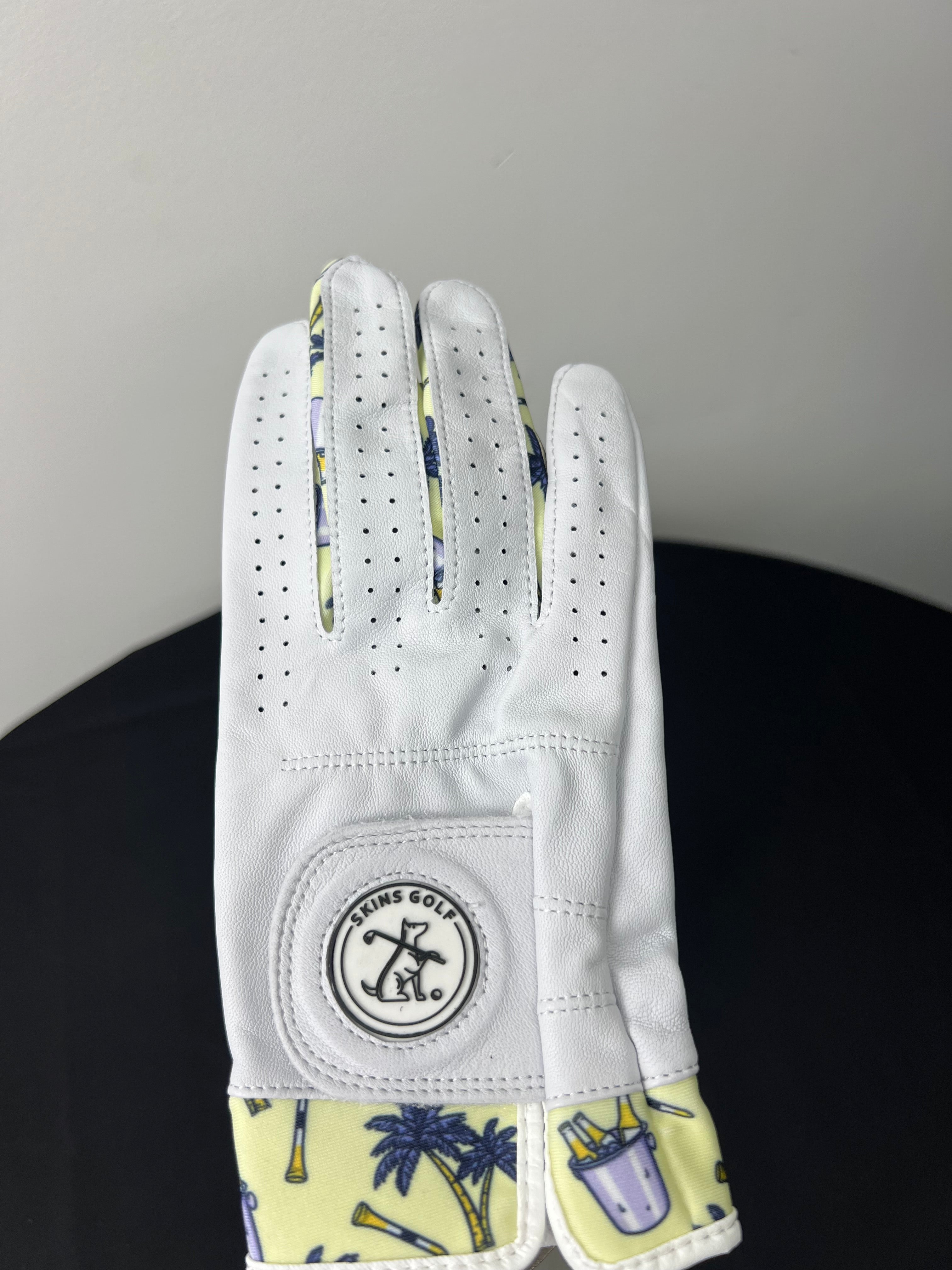 Women's right hand golf glove with palm tree and golf clubs motif at cuff, shown palm up.