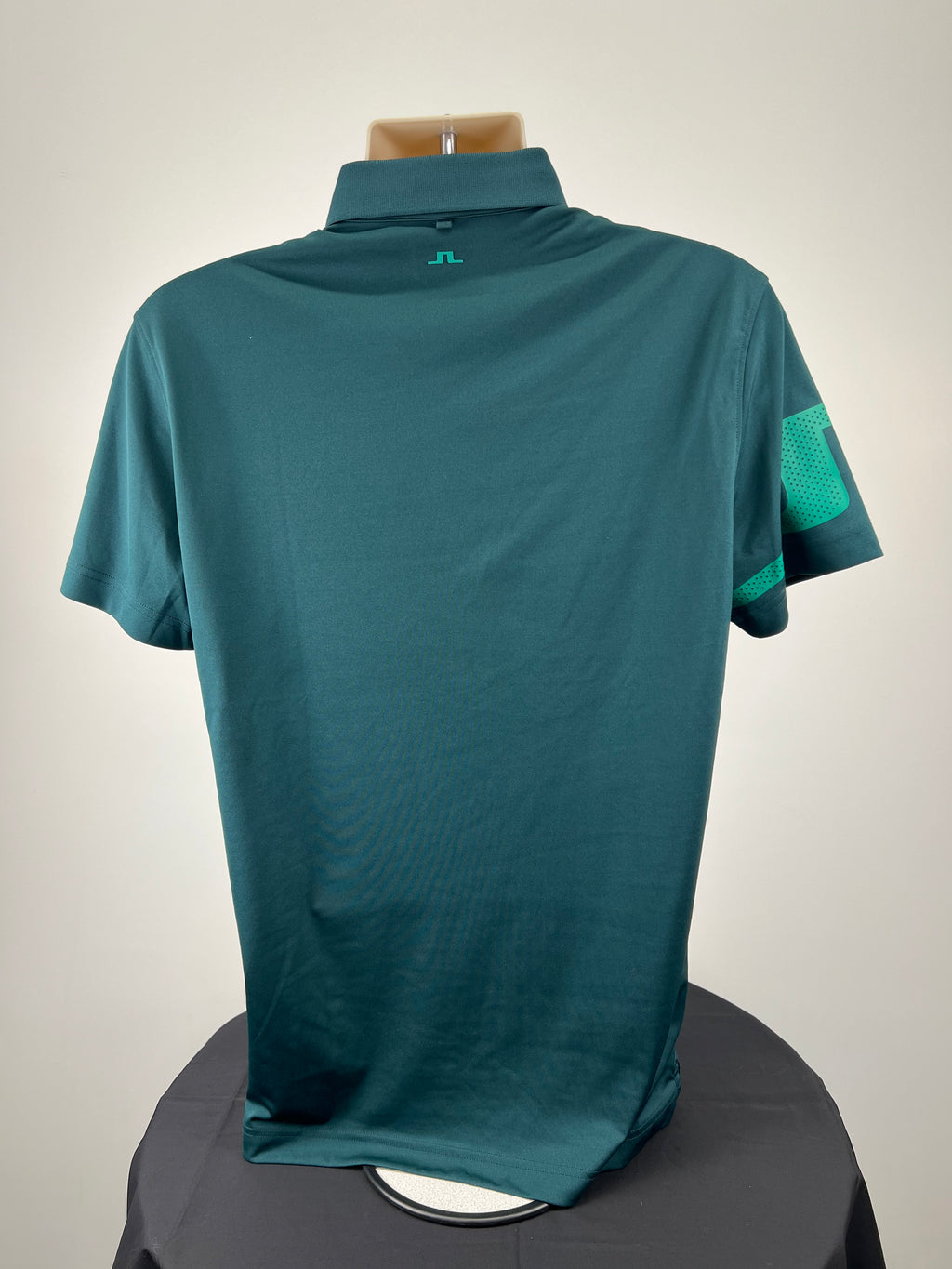 Back view of men’s dark green J. Lindeberg polo shirt showing plain design and teal logo at neckline