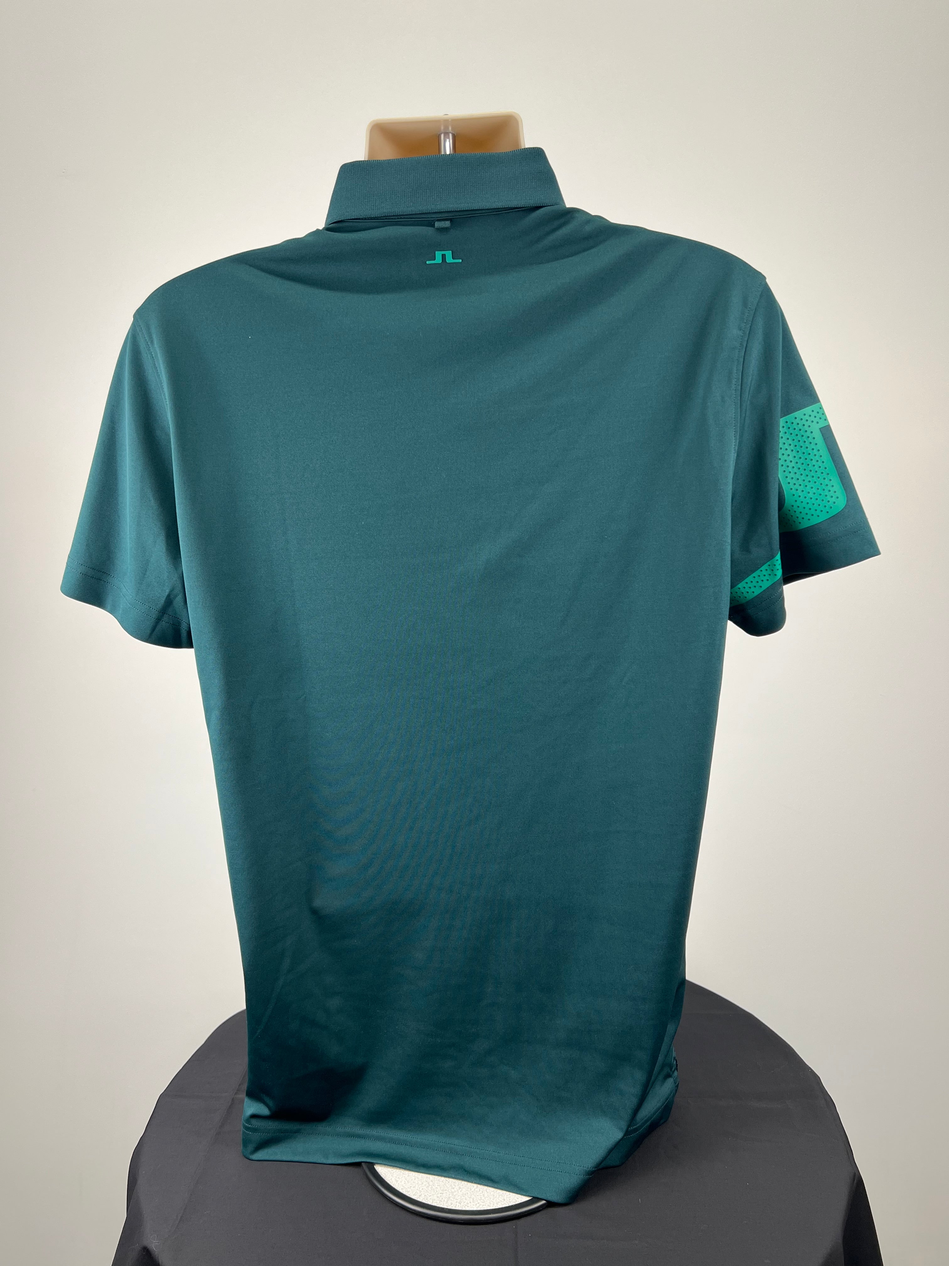 Back view of men’s dark green J. Lindeberg polo shirt showing plain design and teal logo at neckline