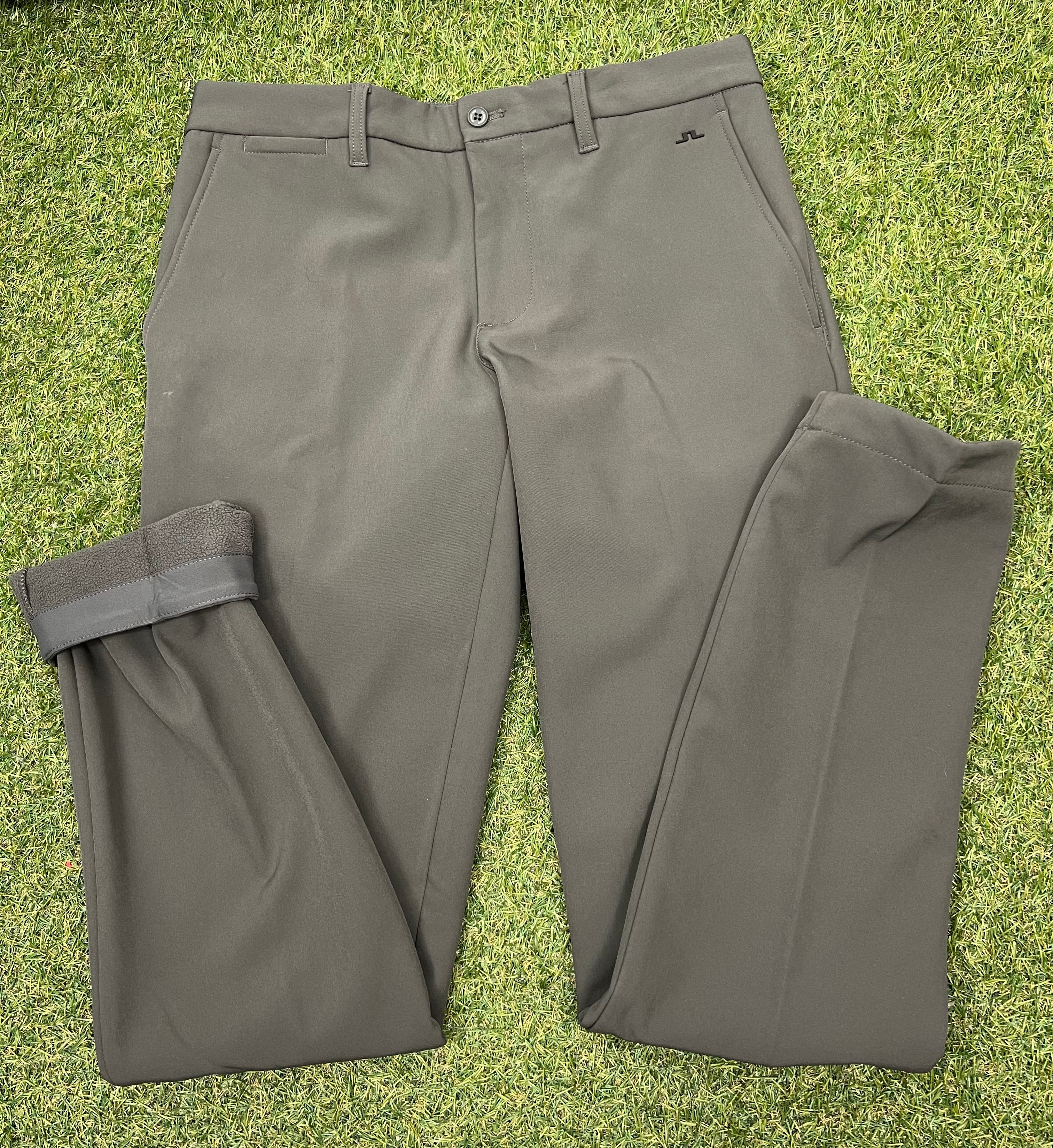 Front view of men’s J.Lindeberg Ellott khaki bonded fleece trousers laid flat on grass showing button and pockets