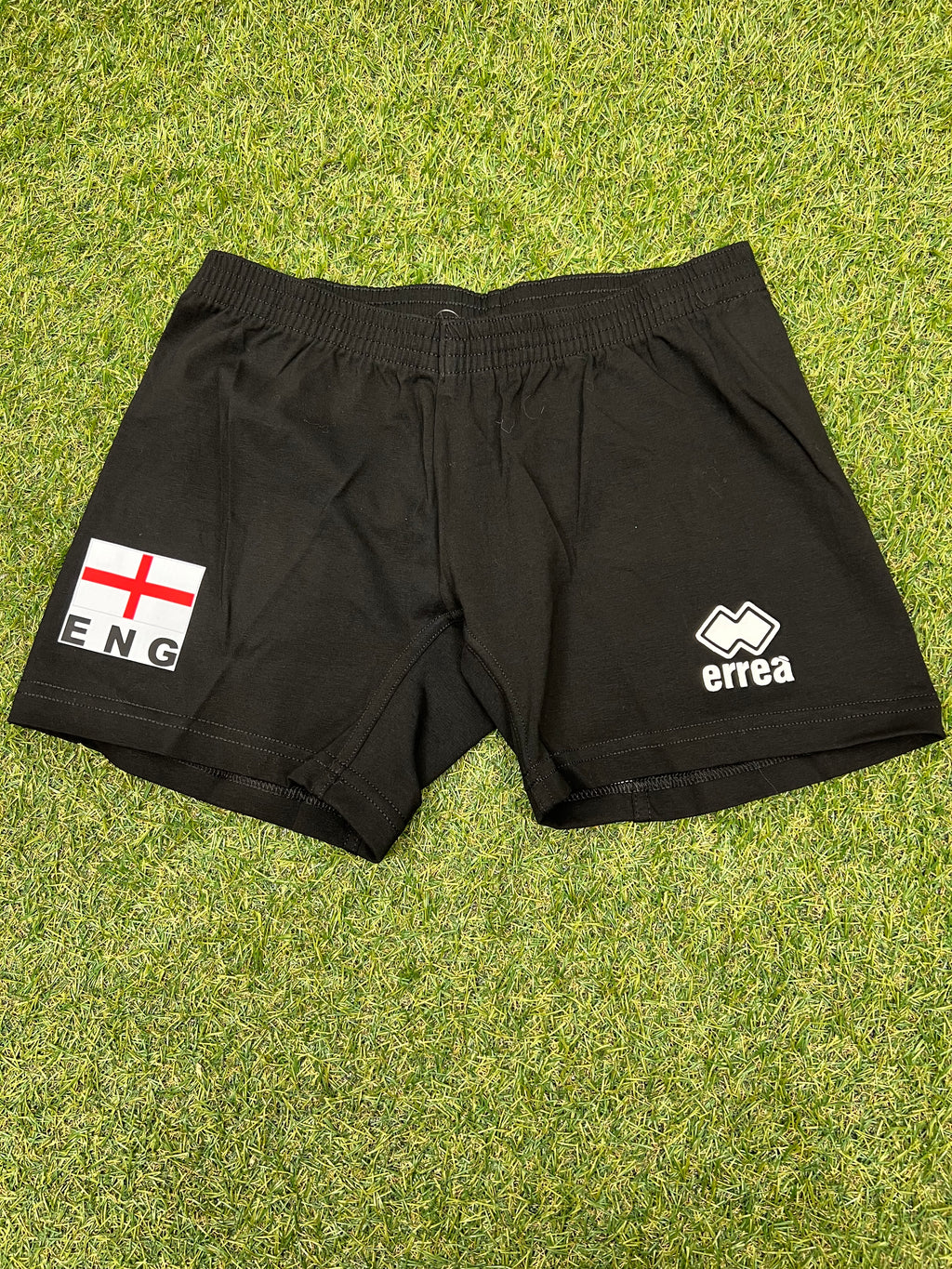 Front view of black Women's volleyball shorts with England flag and Errea logo on grass background